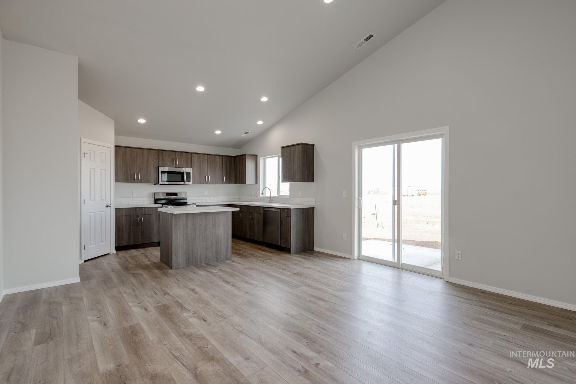 Kitchen with open floor plan, light countertops, a center island, high vaulted ceiling, and light wood-type flooring
