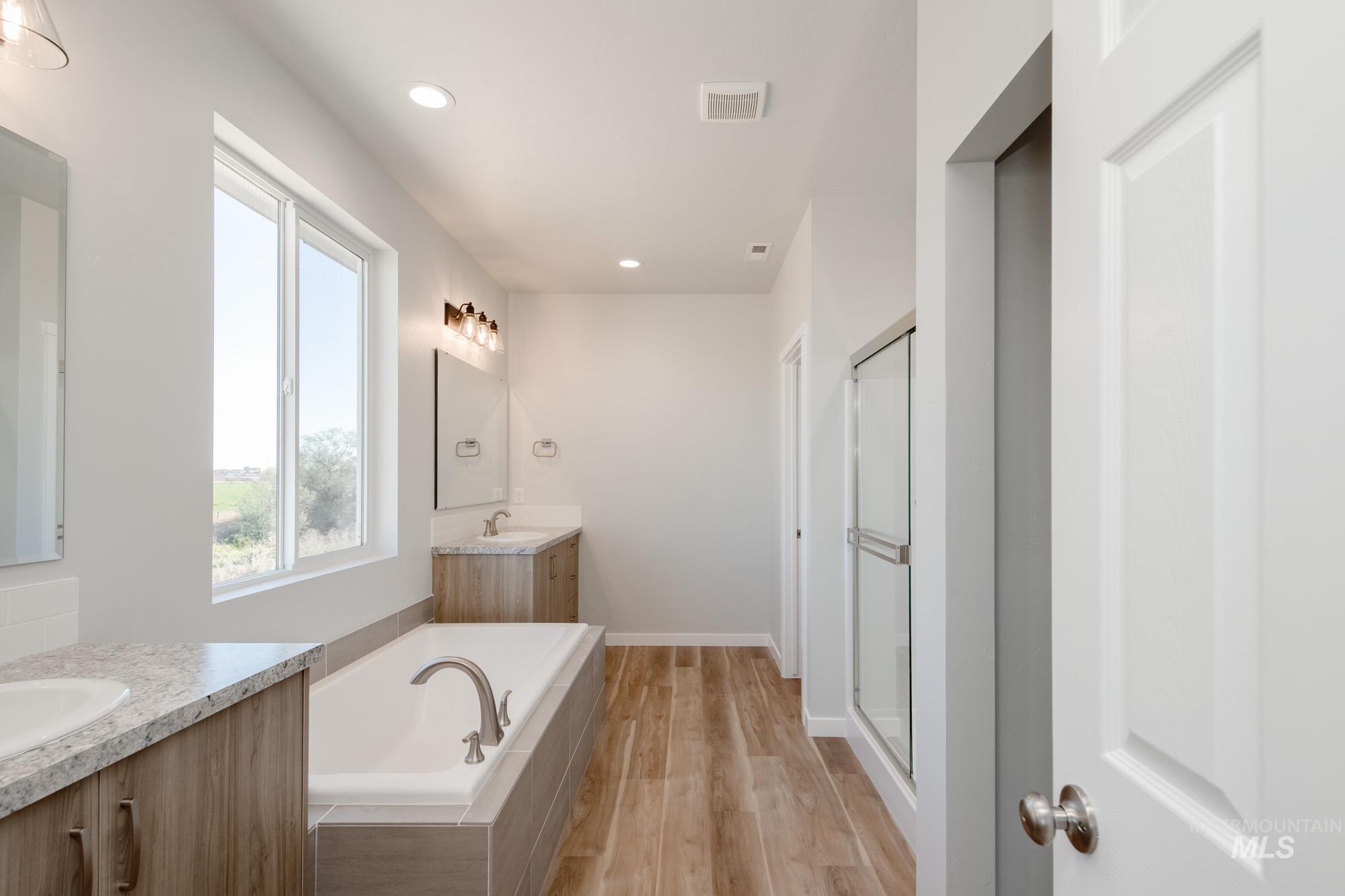 Bathroom with two vanities, a bath, light wood finished floors, a shower stall, and recessed lighting