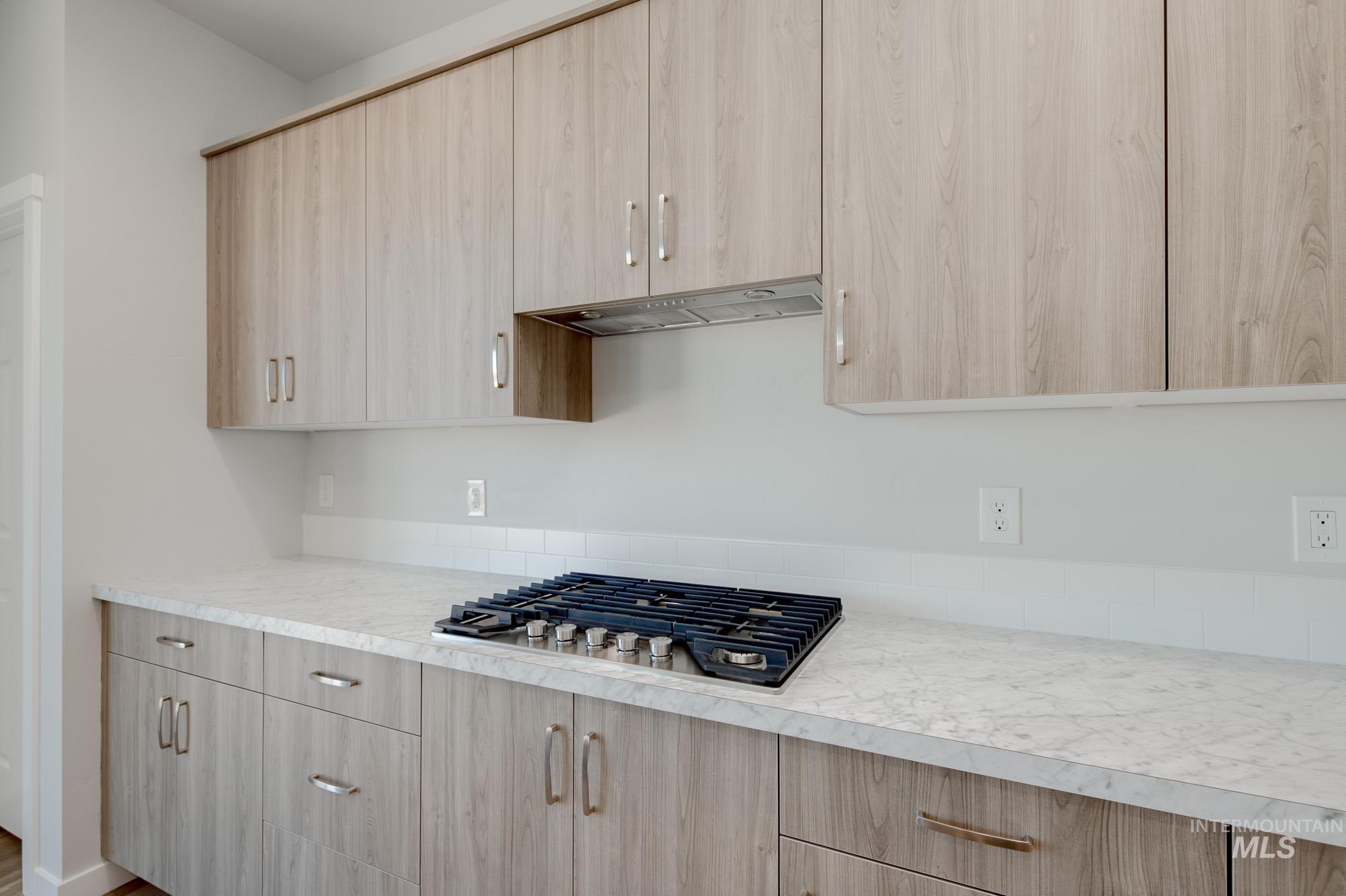 Kitchen featuring light brown cabinetry, light countertops, modern cabinets, stainless steel gas cooktop, and under cabinet range hood