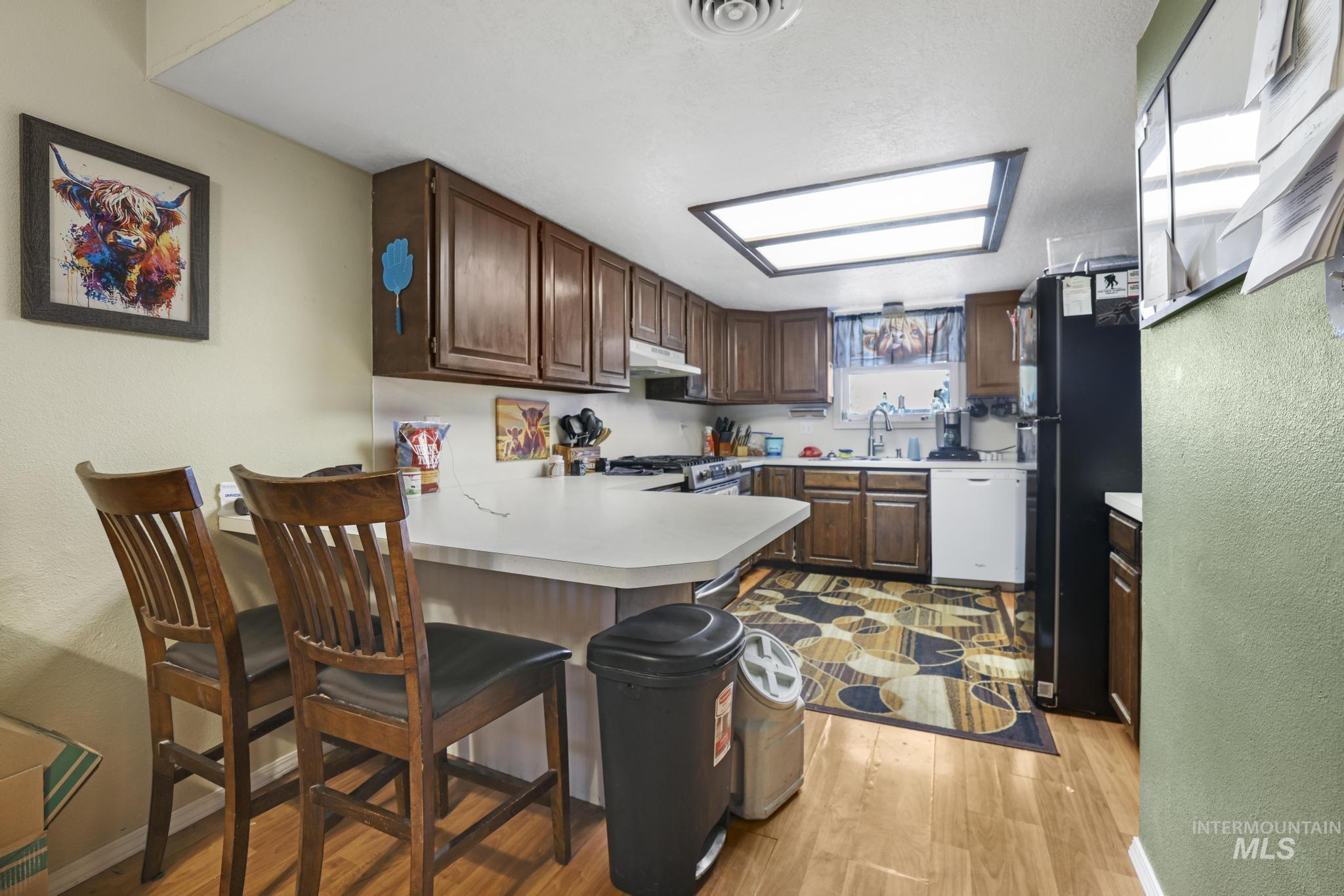 Kitchen featuring a textured wall, light countertops, a peninsula, freestanding refrigerator, and white dishwasher