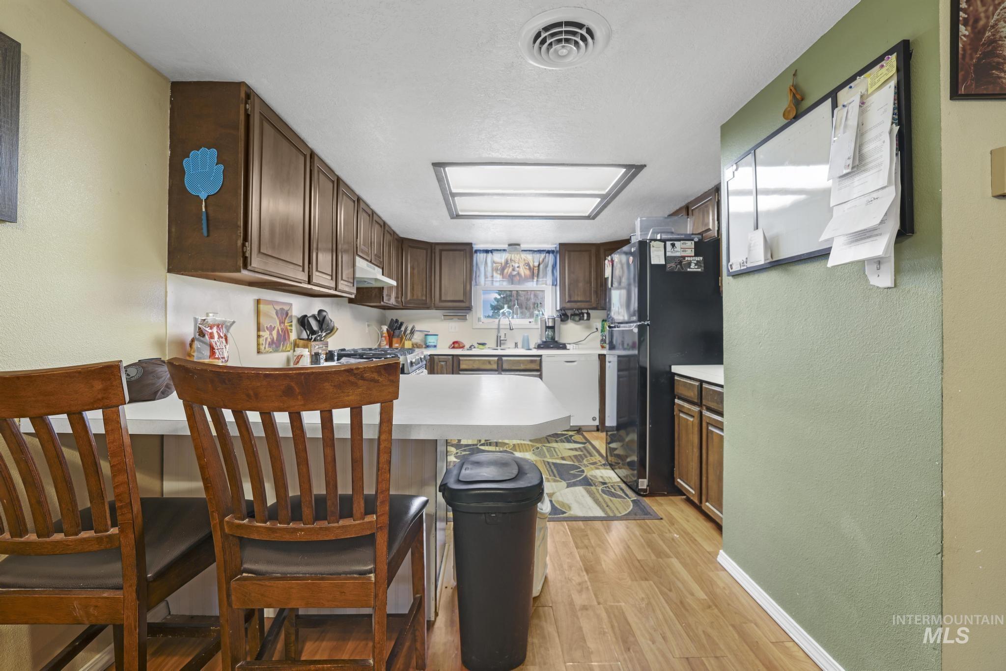Kitchen with a textured wall, light countertops, freestanding refrigerator, a kitchen bar, and a peninsula