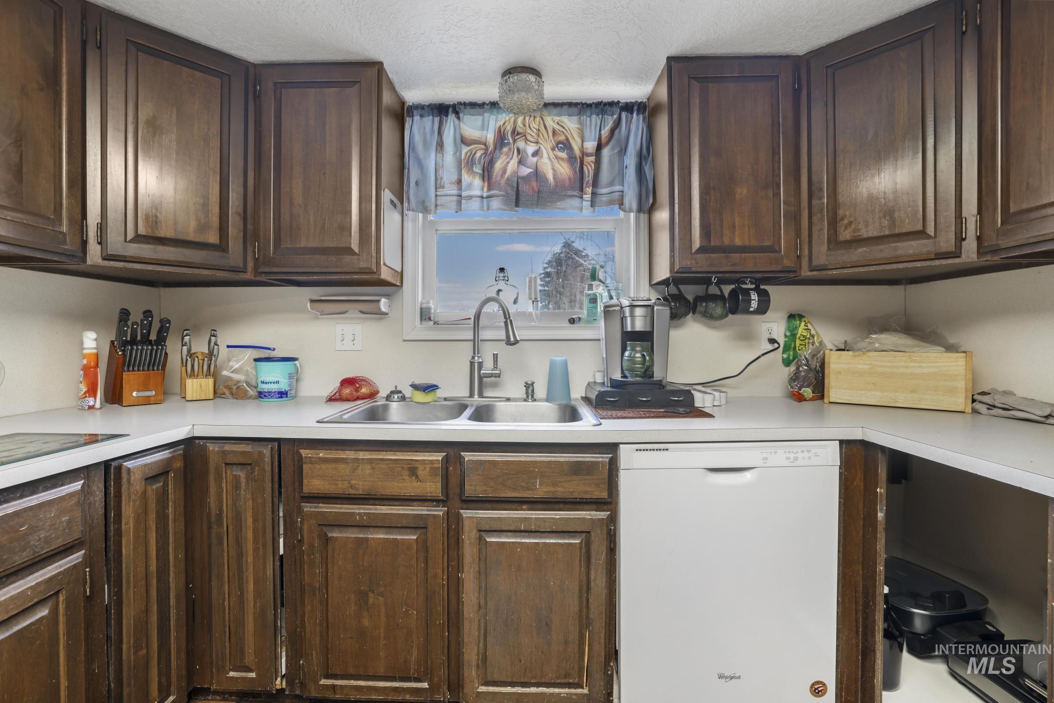 Kitchen featuring dark brown cabinetry, white dishwasher, light countertops, and a chandelier