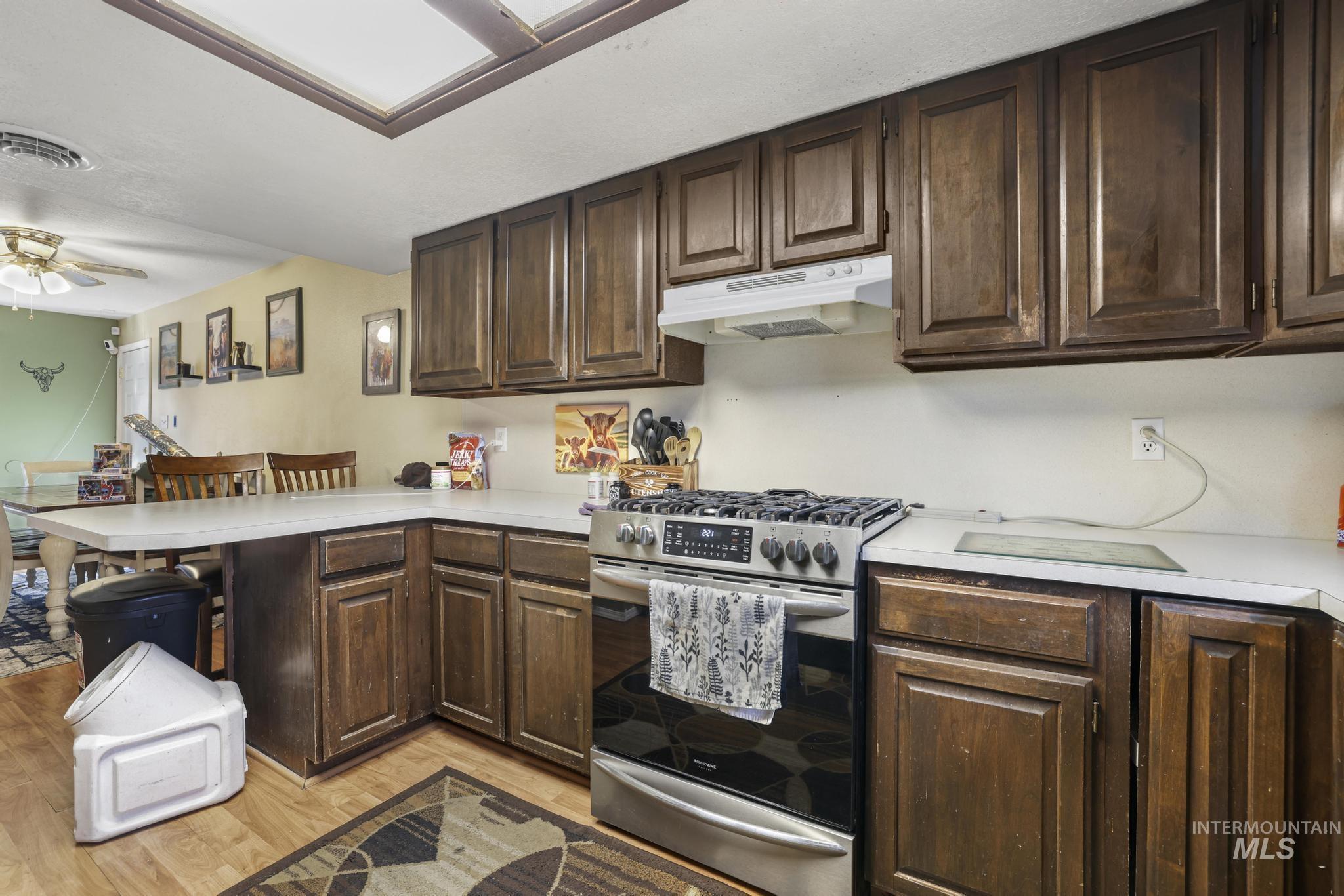 Kitchen with dark brown cabinets, stainless steel gas range, a peninsula, light countertops, and under cabinet range hood