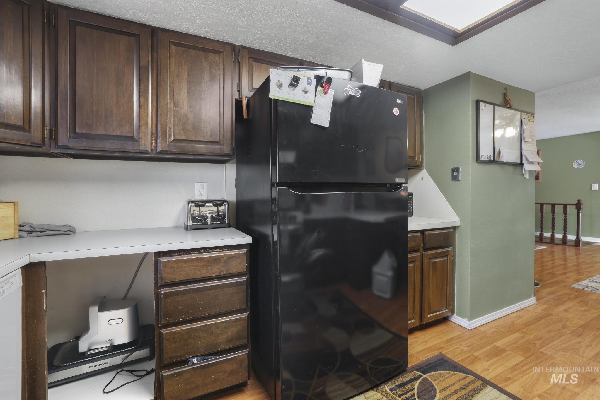 Kitchen featuring freestanding refrigerator, light countertops, light wood-style floors, and dark brown cabinets