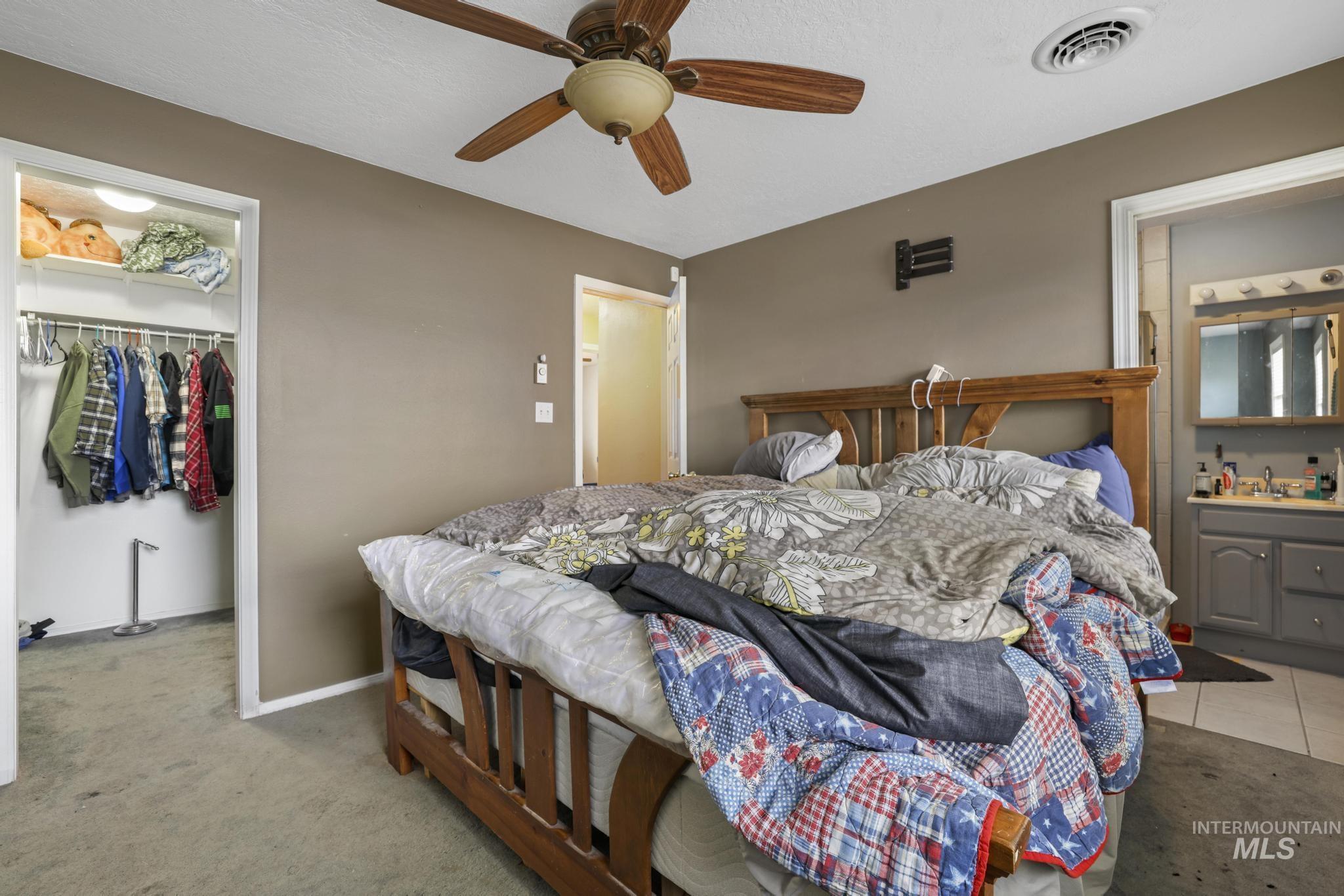 Bedroom featuring a walk in closet, ensuite bath, light colored carpet, and ceiling fan
