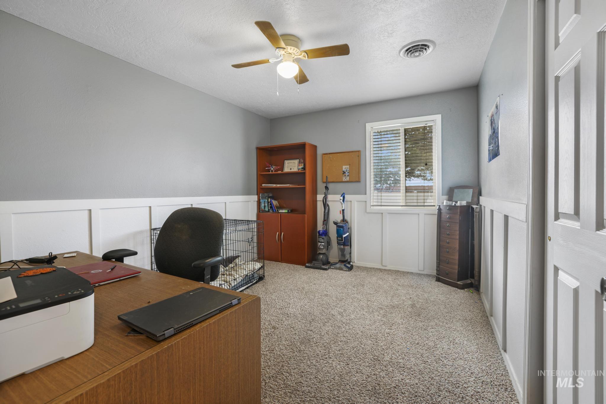 Office space with a decorative wall, light colored carpet, a wainscoted wall, and ceiling fan