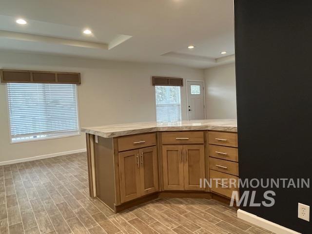Kitchen featuring brown cabinetry, recessed lighting, wood tiled floors, a tray ceiling, and a peninsula