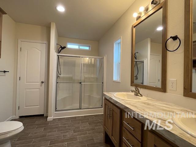Bathroom with double vanity, a stall shower, wood finish floors, and recessed lighting