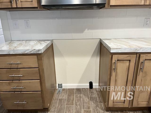 Detailed view of brown cabinetry, light countertops, tasteful backsplash, and wood tiled floors