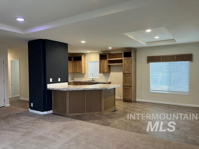 Kitchen featuring a tray ceiling, a peninsula, recessed lighting, dark colored carpet, and brown cabinets