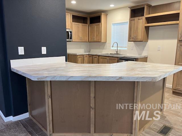 Kitchen featuring a peninsula, light countertops, stainless steel microwave, decorative backsplash, and recessed lighting