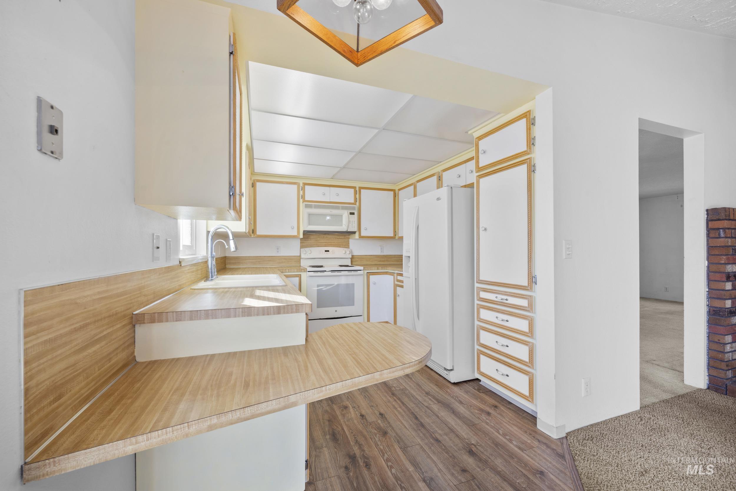 Kitchen with light countertops, white appliances, a peninsula, and dark wood finished floors