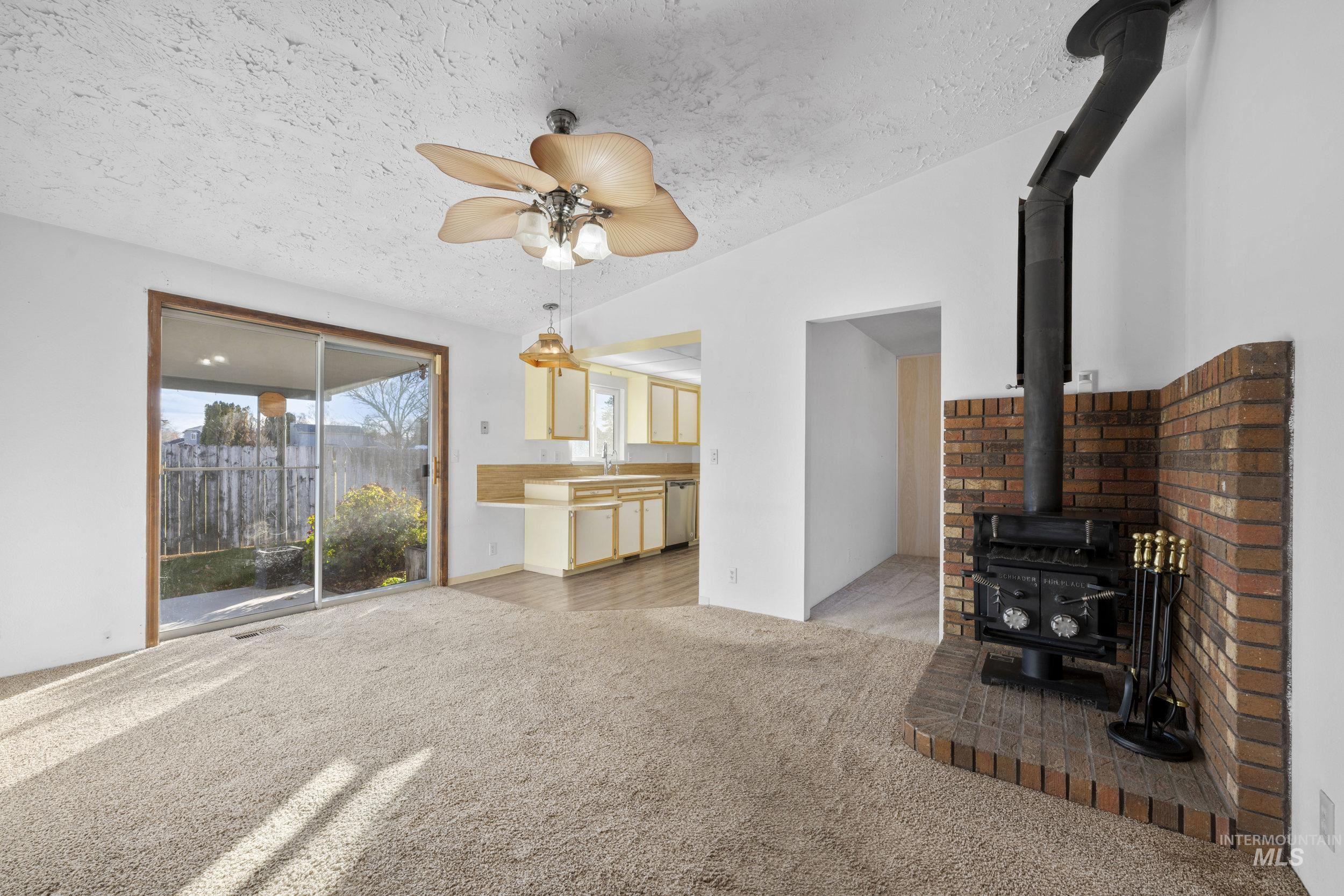 Unfurnished living room with a wood stove, light colored carpet, a textured ceiling, a ceiling fan, and vaulted ceiling