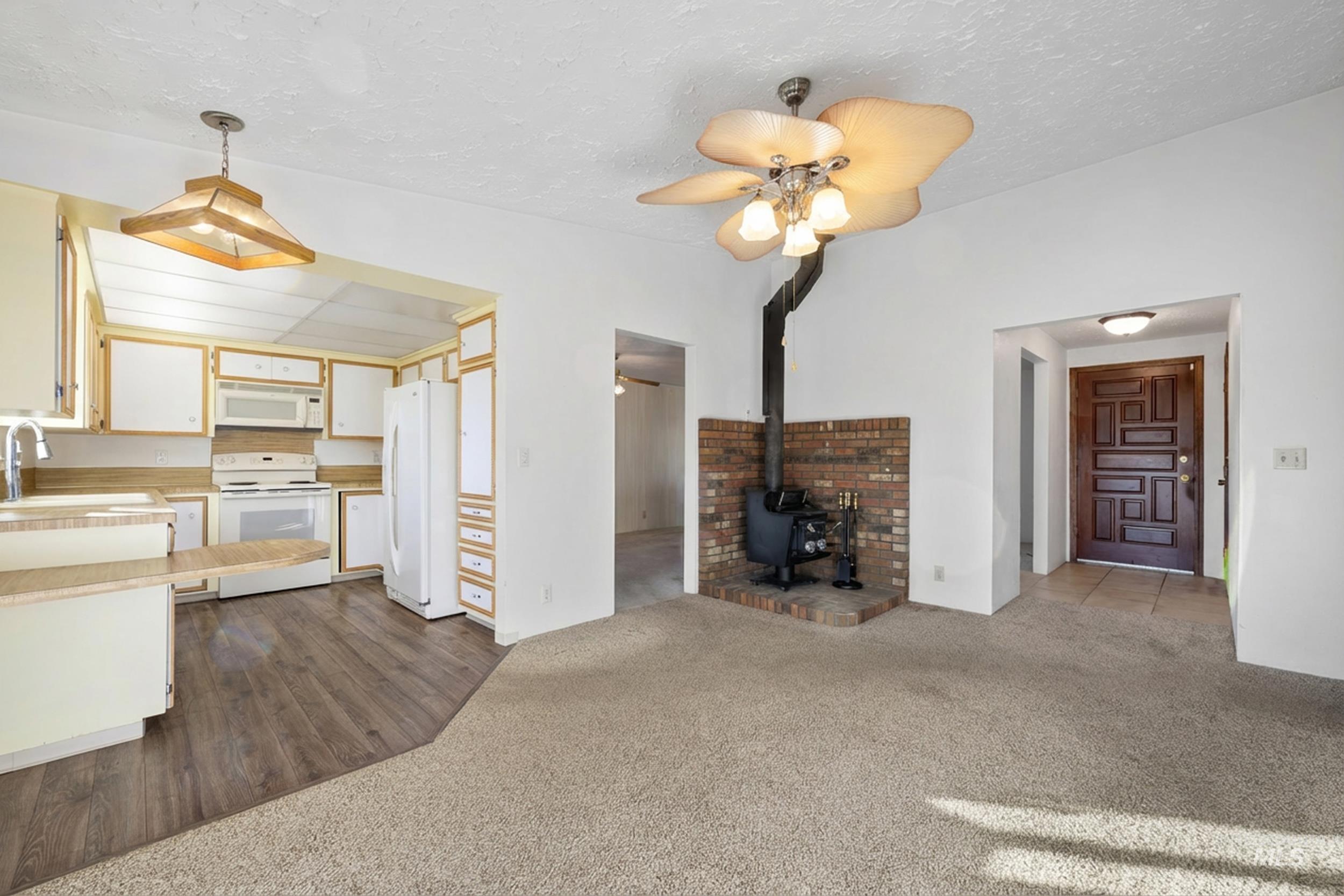 Kitchen with a wood stove, light countertops, dark colored carpet, white appliances, and ceiling fan