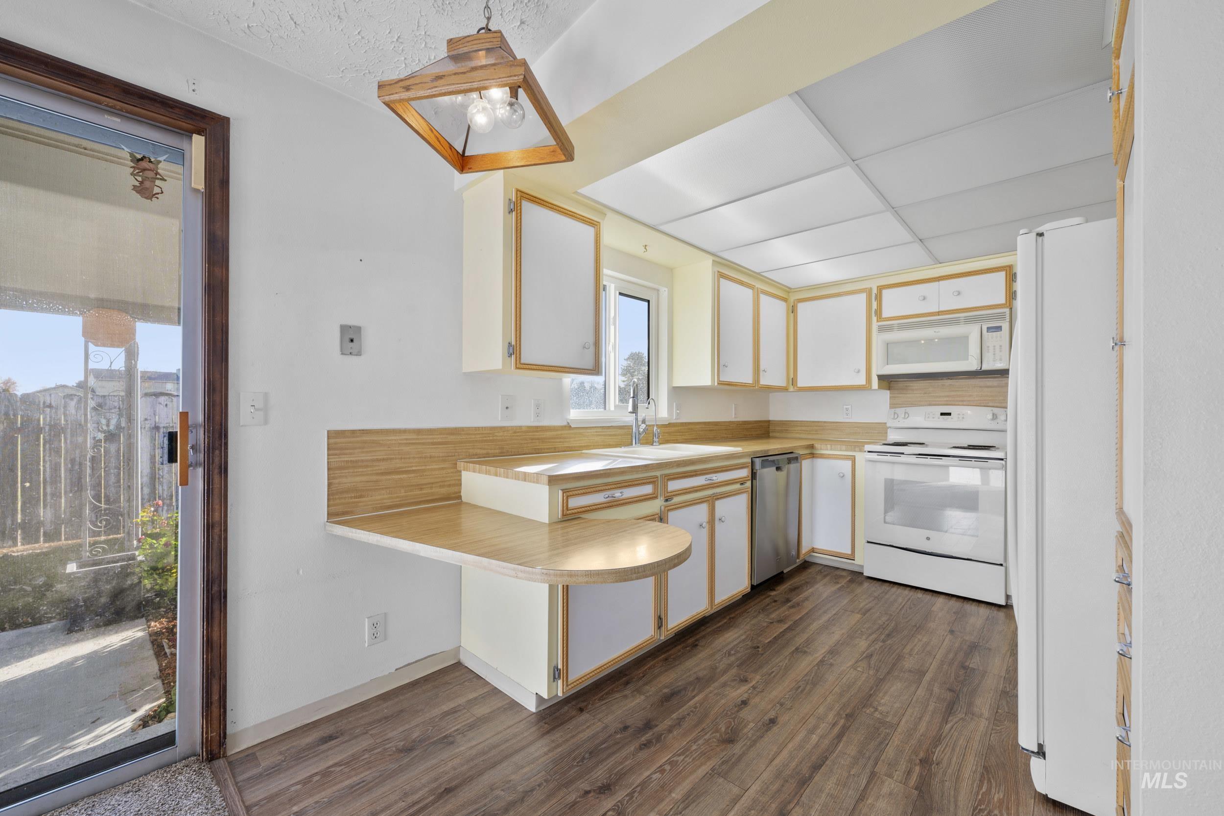 Kitchen with light countertops, white appliances, white cabinets, hanging light fixtures, and dark wood-style floors