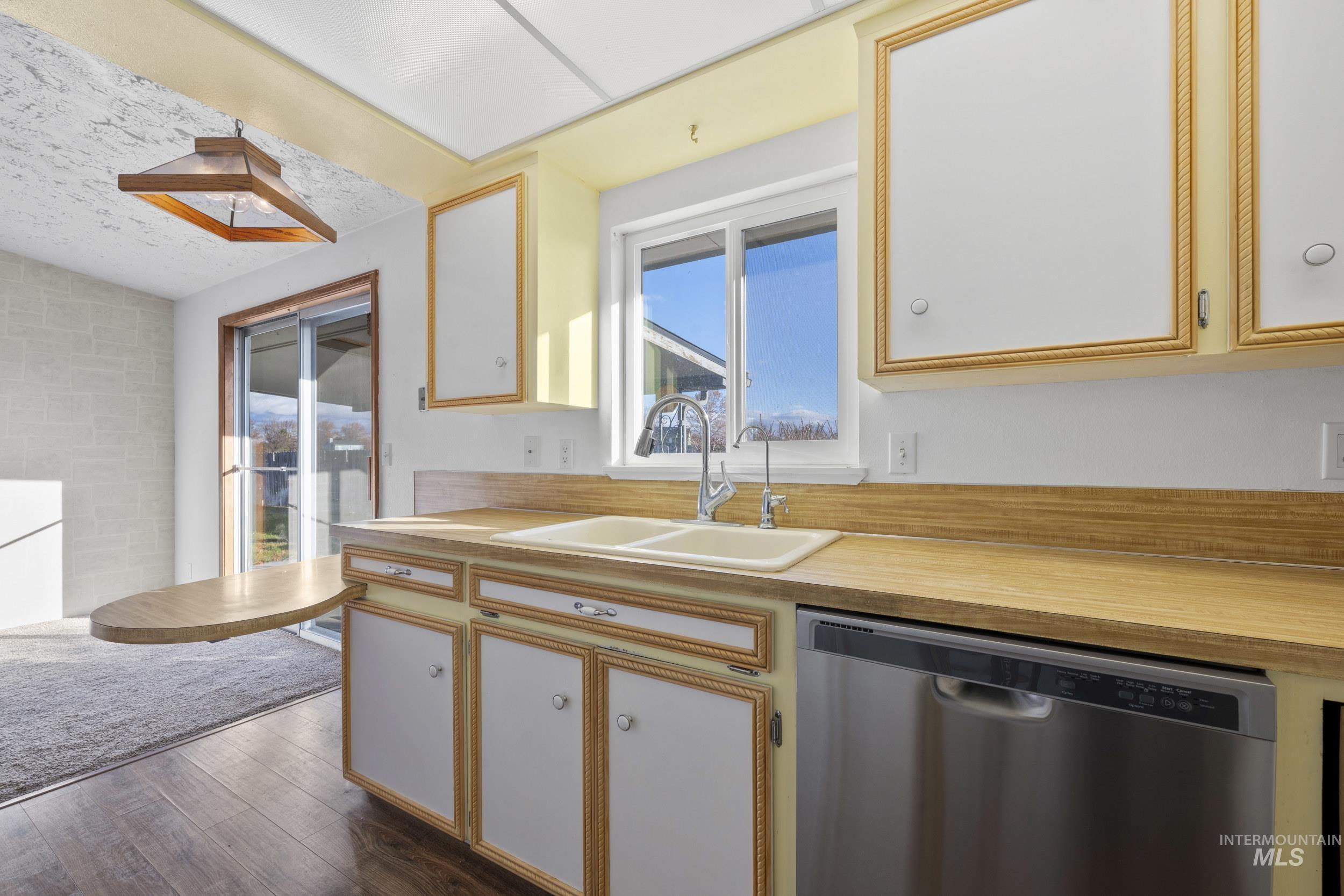 Kitchen with dishwasher, light countertops, white cabinets, and dark wood-style flooring