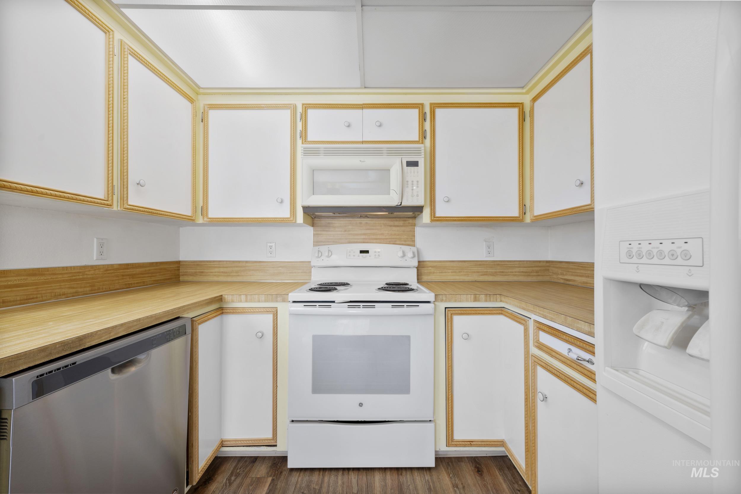 Kitchen with white appliances, light countertops, white cabinets, and dark wood-style flooring