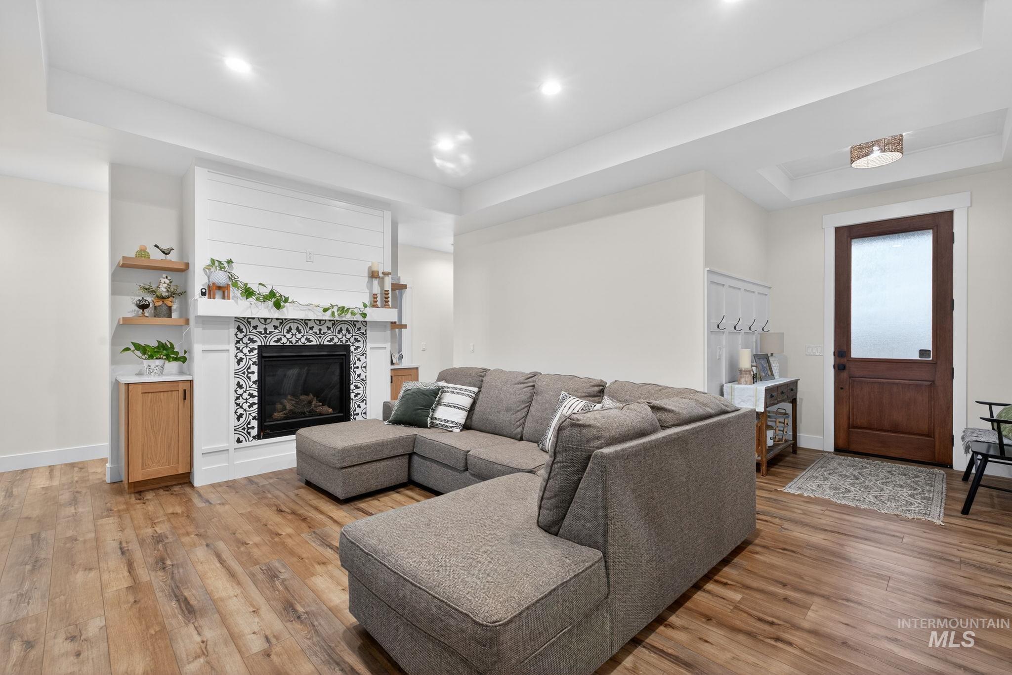 Living area featuring a raised ceiling, light wood-style floors, a tile fireplace, and recessed lighting