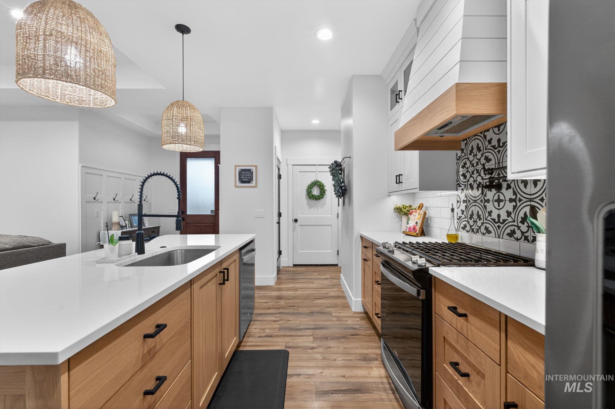 Kitchen with stainless steel appliances, recessed lighting, light wood-type flooring, light stone countertops, and custom exhaust hood