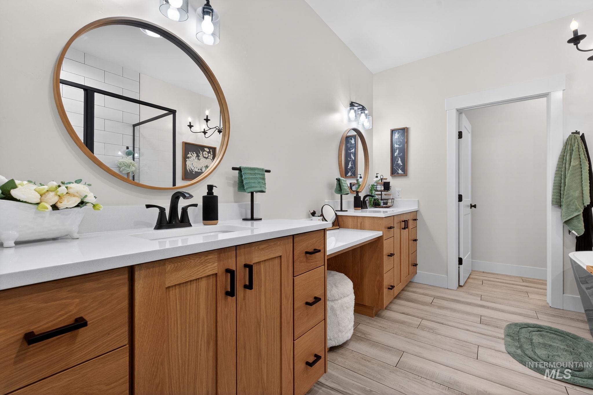 Full bathroom featuring two vanities, wood finish floors, and a stall shower