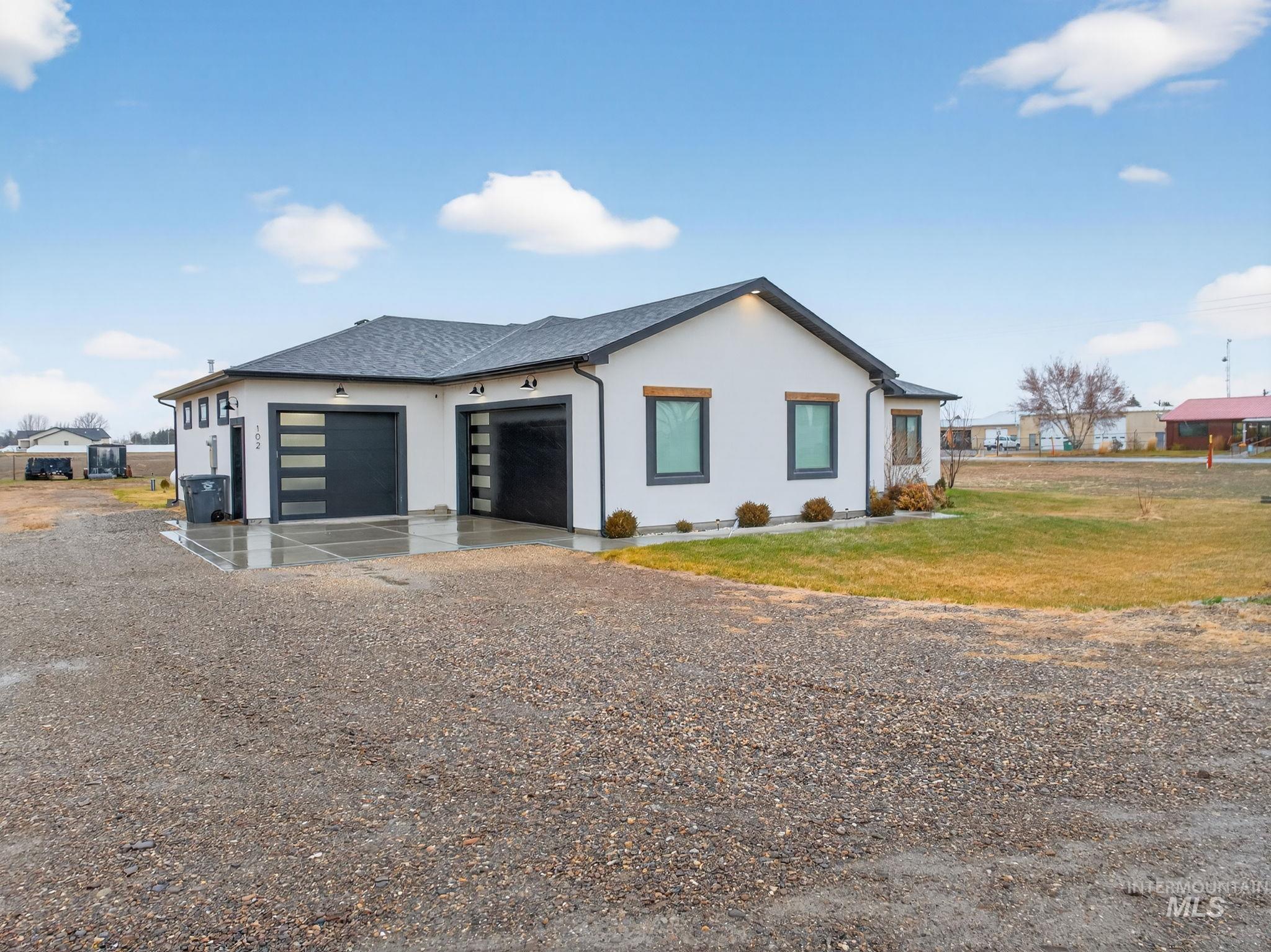 View of front of home featuring gravel driveway, stucco siding, an attached garage, and roof with shingles
