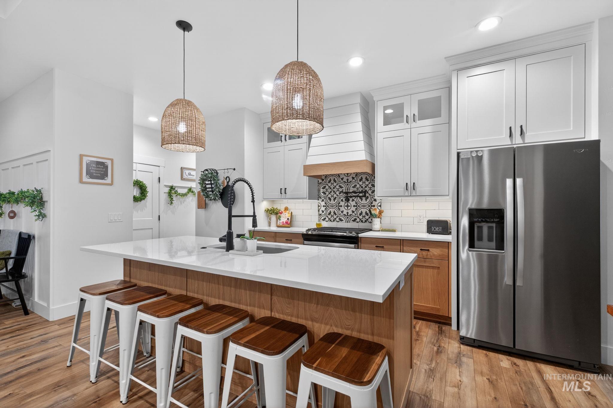 Kitchen featuring glass insert cabinets, appliances with stainless steel finishes, brown cabinetry, a kitchen breakfast bar, and a kitchen island with sink