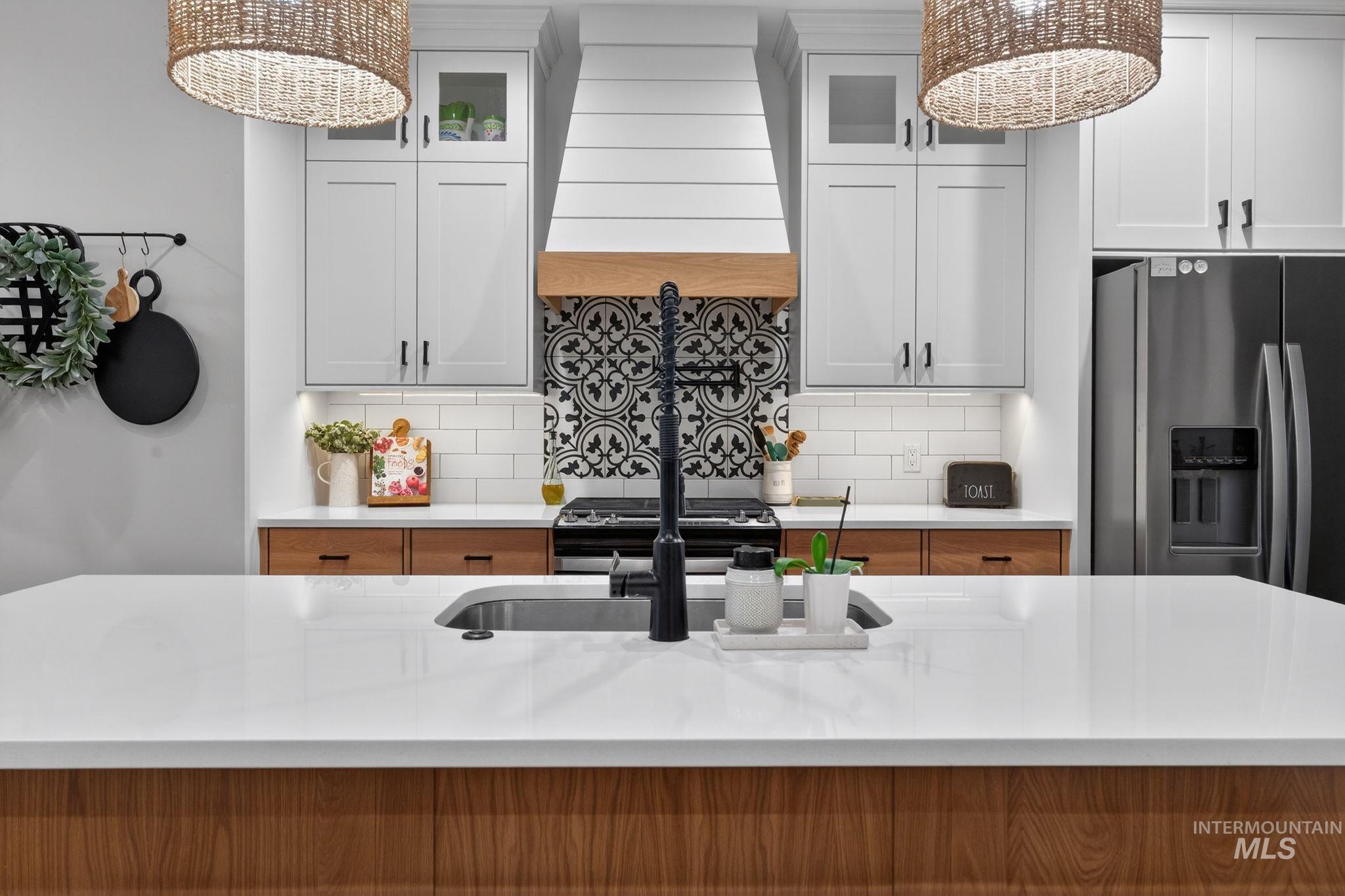 Kitchen with premium range hood, glass insert cabinets, white cabinetry, stainless steel fridge, and a chandelier
