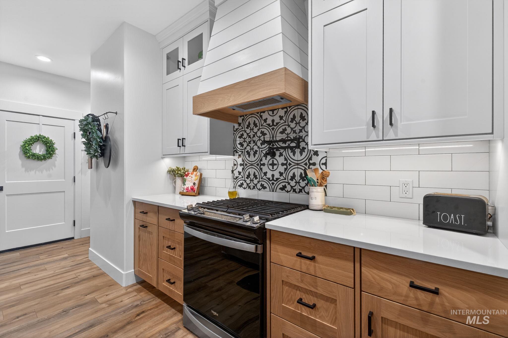 Kitchen with stainless steel range with gas stovetop, premium range hood, white cabinetry, glass insert cabinets, and light wood-style floors