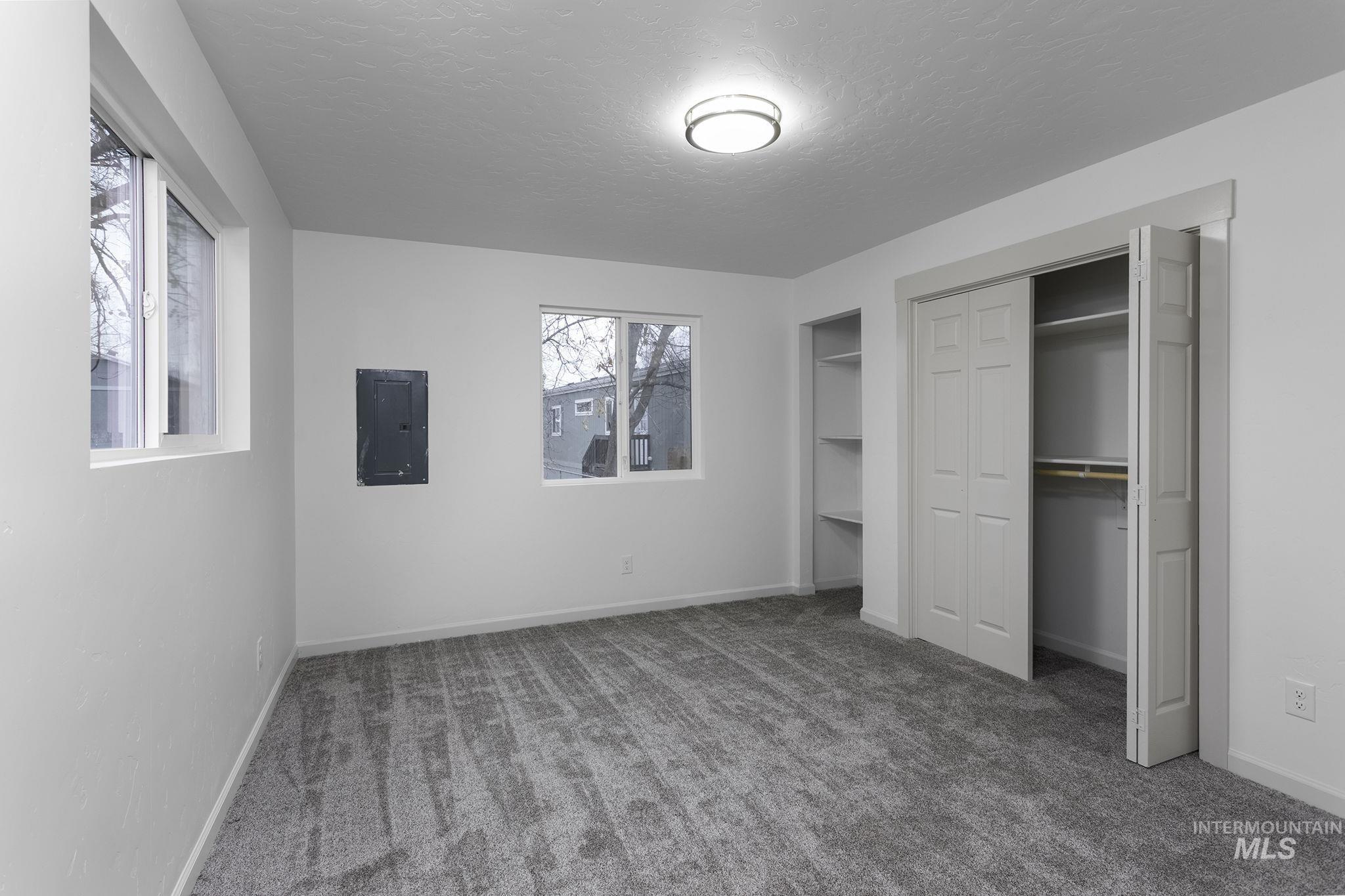 Unfurnished bedroom featuring carpet flooring, a textured ceiling, electric panel, and multiple closets