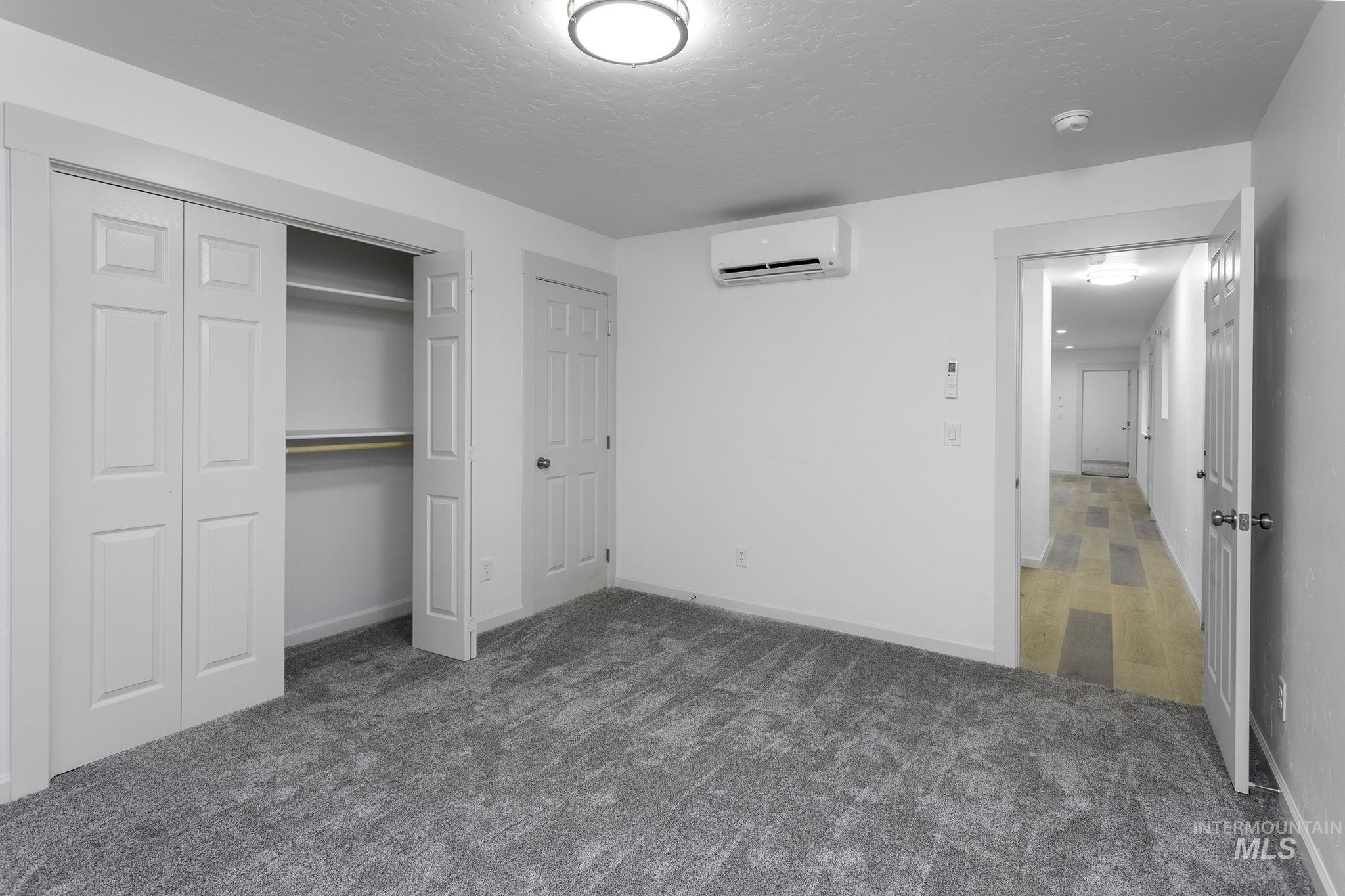 Unfurnished bedroom with dark carpet, a closet, a textured ceiling, and a wall mounted AC