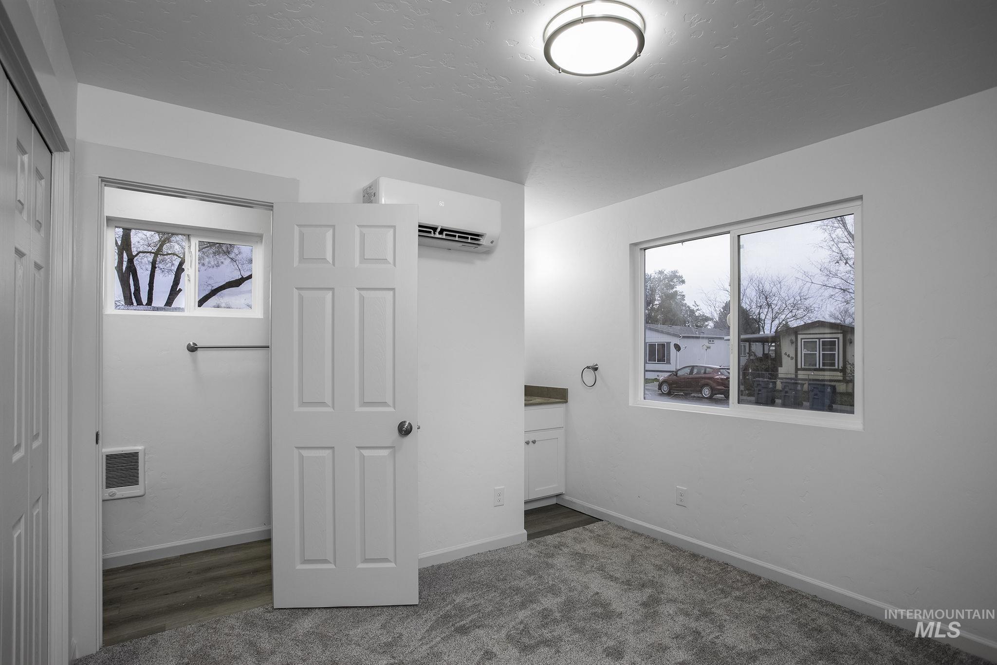 Unfurnished bedroom featuring a closet, a wall unit AC, dark carpet, heating unit, and a textured ceiling