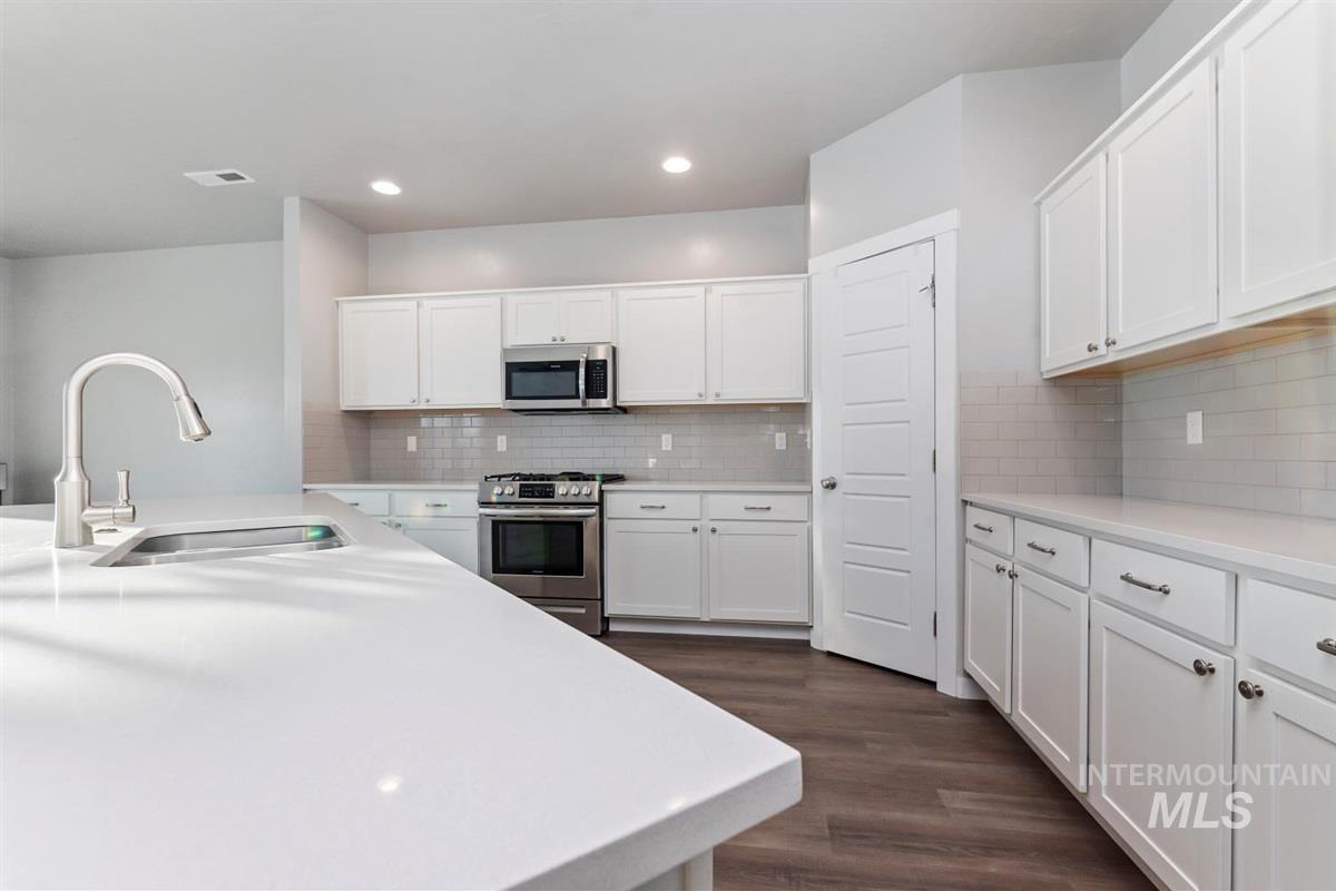Kitchen with white cabinets, stainless steel appliances, decorative backsplash, dark wood finished floors, and recessed lighting