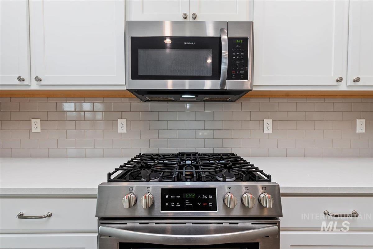 Kitchen view of appliances with stainless steel finishes, white cabinetry, and decorative backsplash