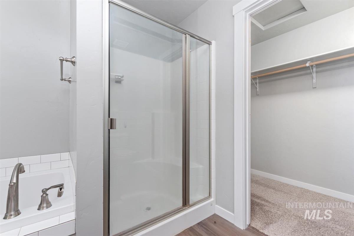 Full bathroom featuring a shower stall, a garden tub, a walk in closet, and wood finished floors