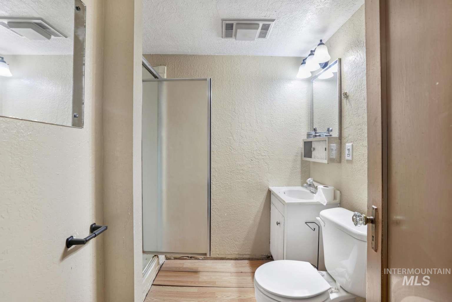 Full bath with a textured wall, vanity, light wood-type flooring, a stall shower, and a textured ceiling