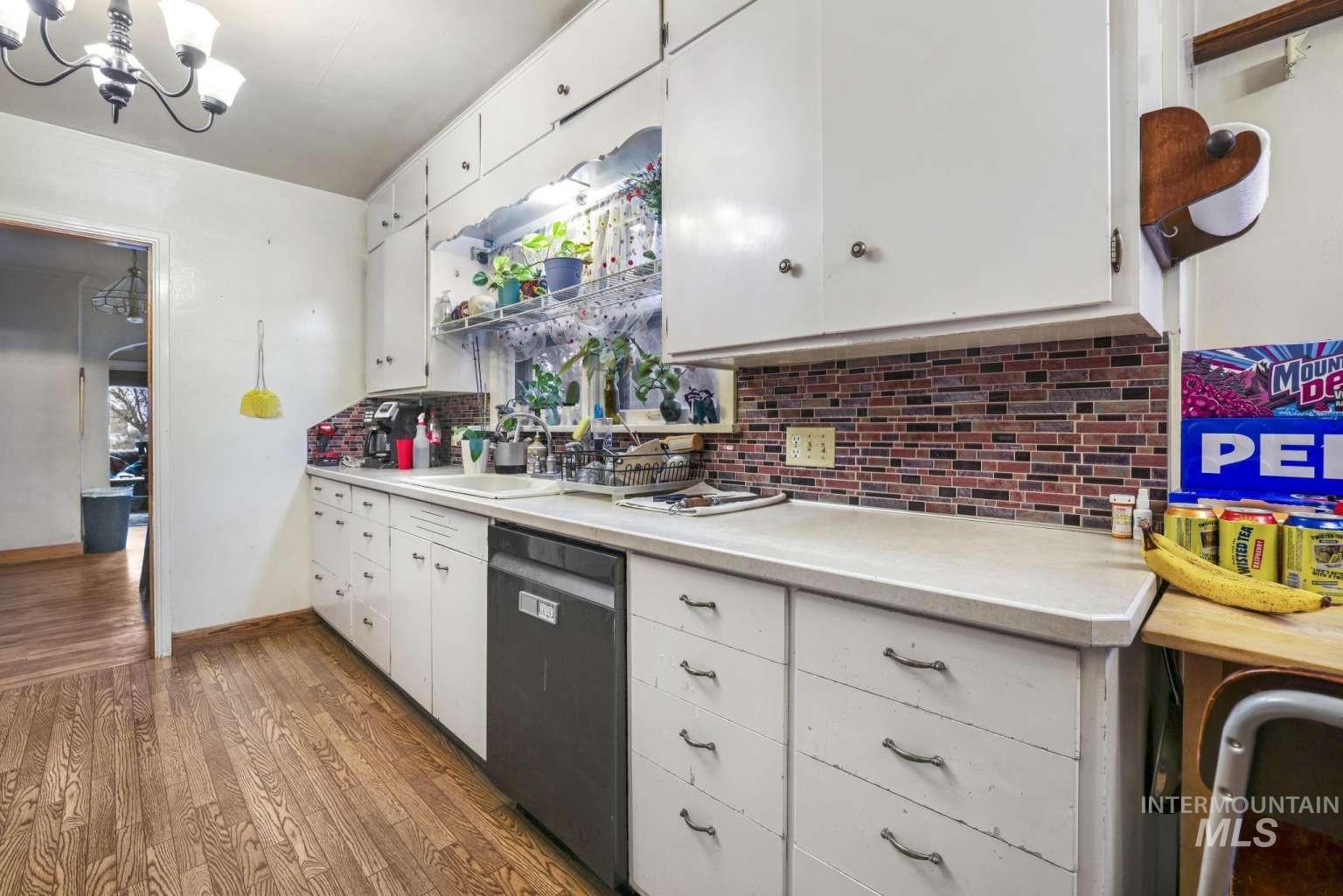Kitchen featuring light countertops, tasteful backsplash, dishwasher, white cabinets, and wood finished floors
