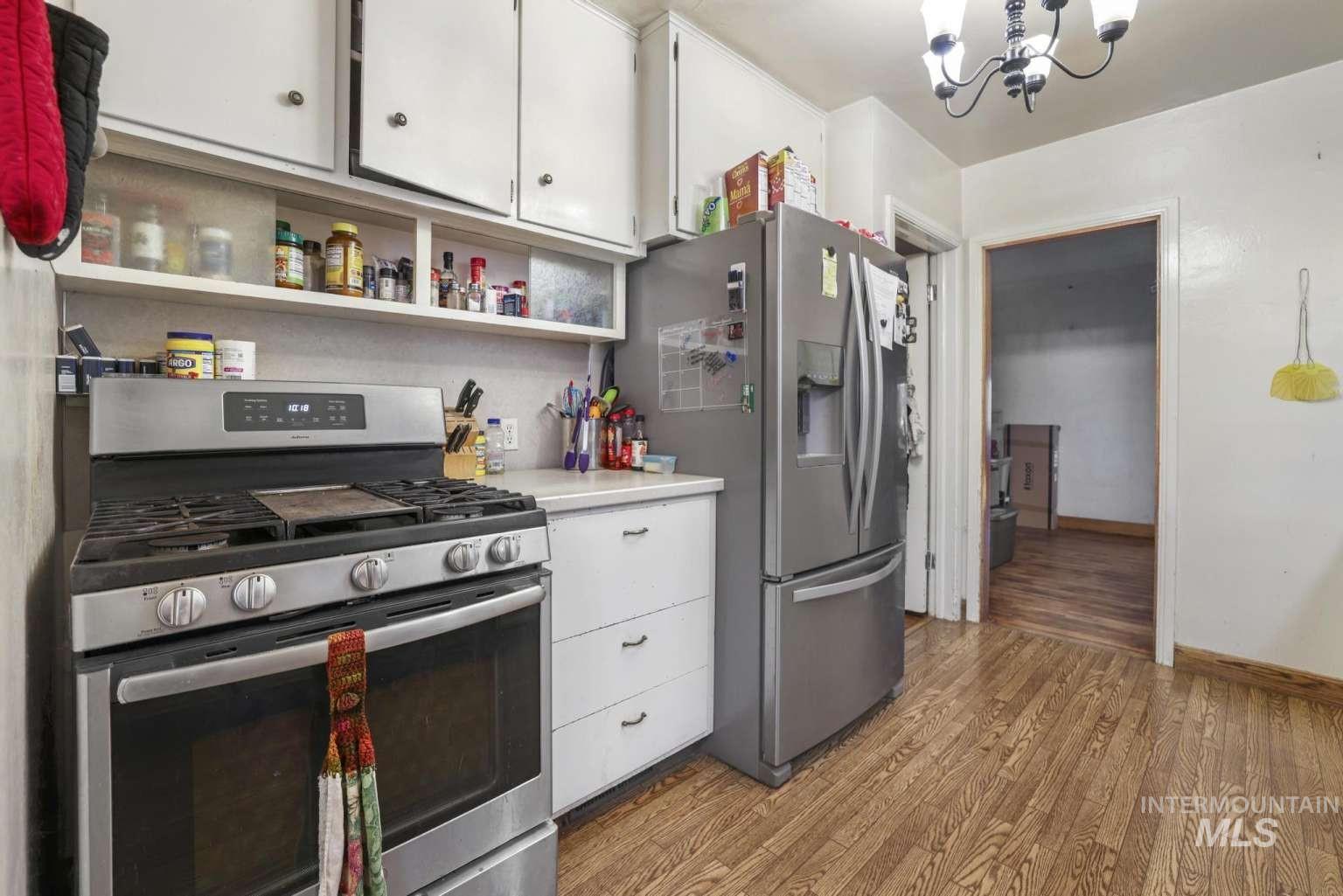 Kitchen with white cabinets, appliances with stainless steel finishes, light countertops, a chandelier, and light wood-style flooring