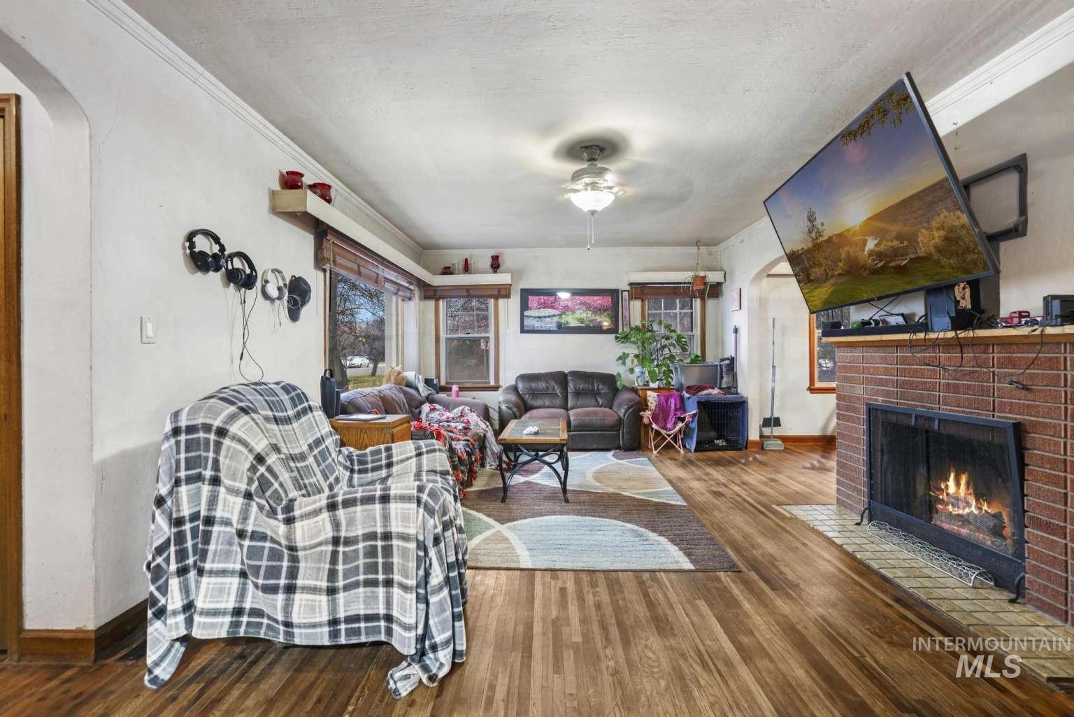 Living area featuring arched walkways, wood finished floors, ornamental molding, a brick fireplace, and a ceiling fan