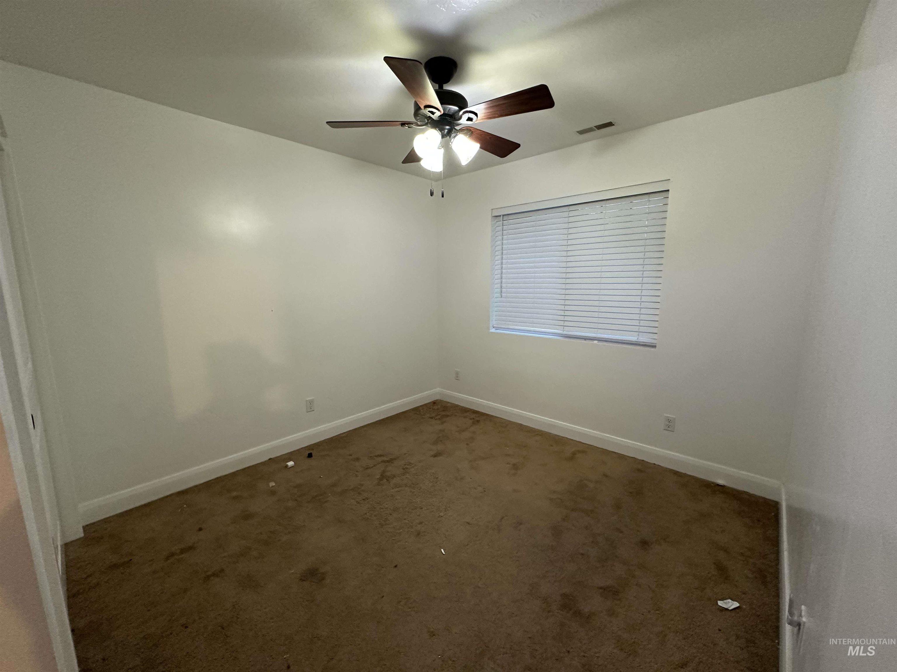 Empty room with dark colored carpet and a ceiling fan