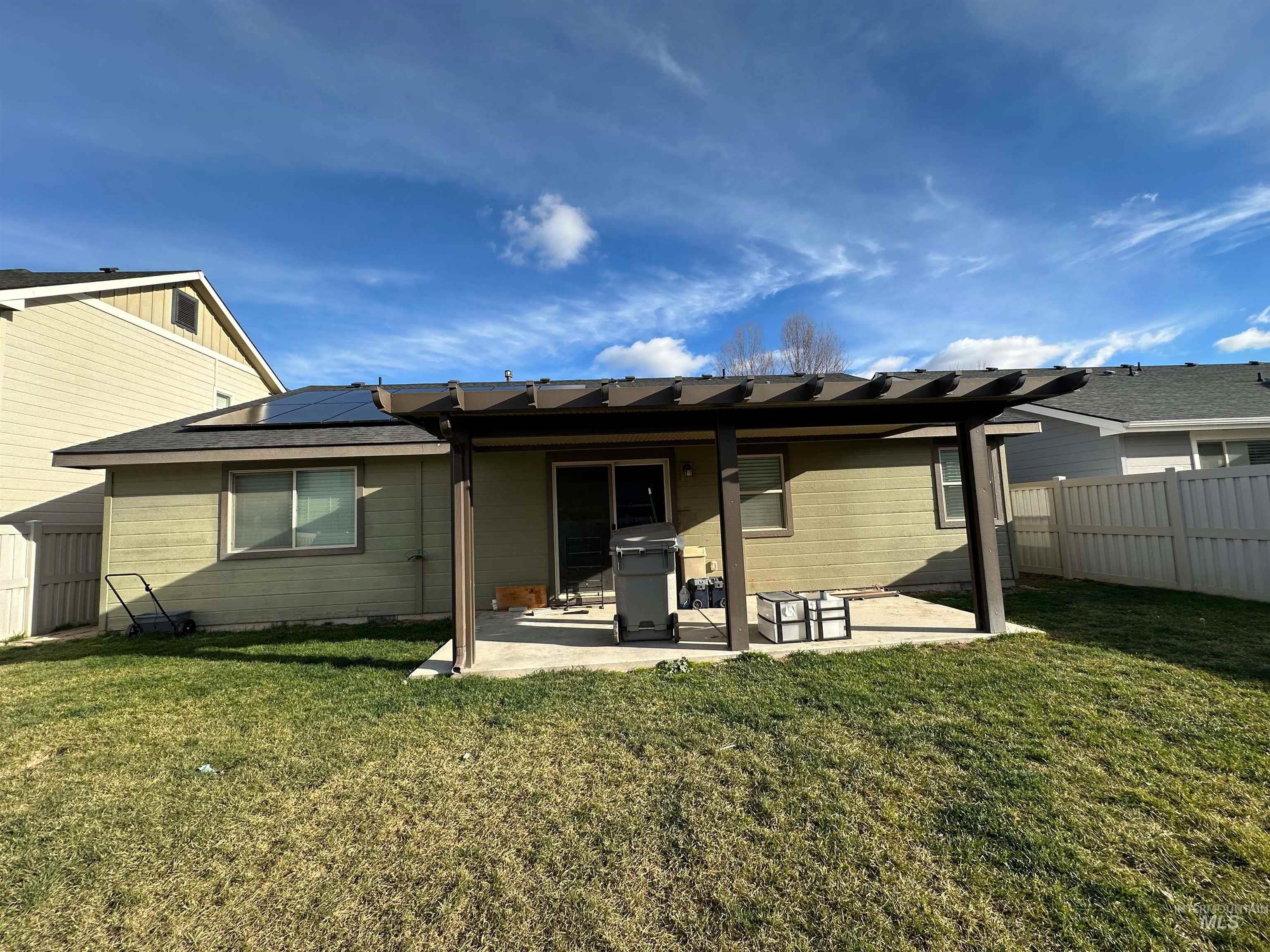 Rear view of house featuring a patio, roof mounted solar panels, and a fenced backyard
