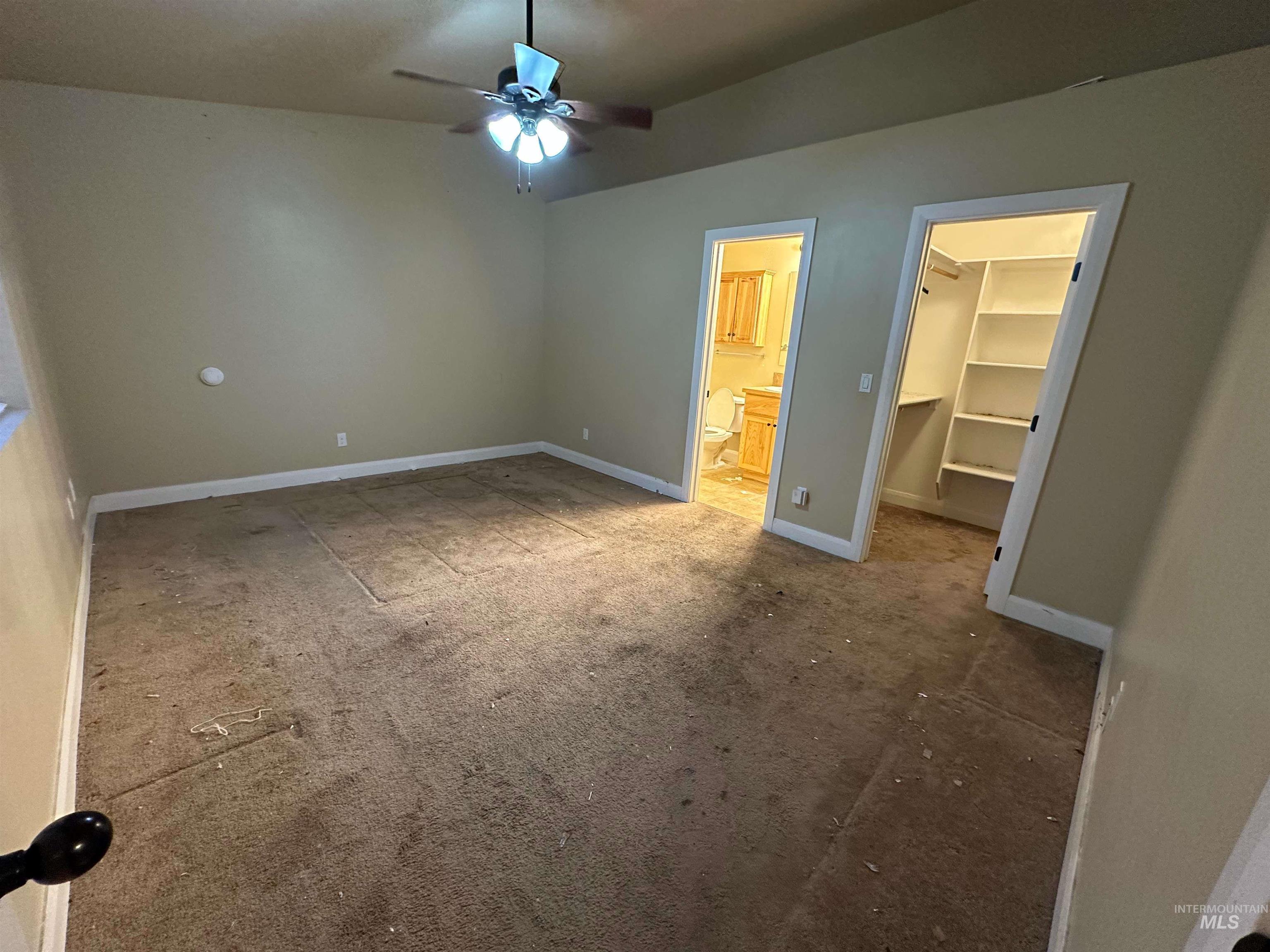 Unfurnished bedroom featuring a spacious closet, light colored carpet, a ceiling fan, and ensuite bath