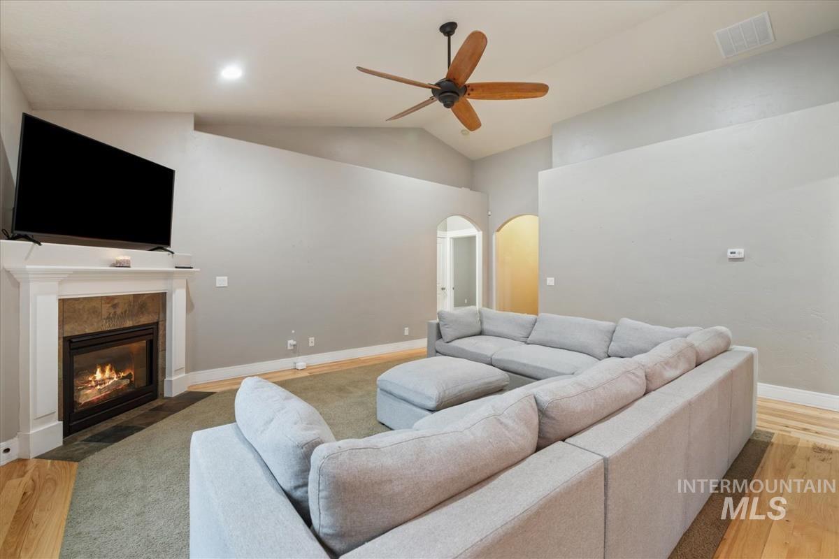 Living room with light wood-style flooring, arched walkways, lofted ceiling, a tiled fireplace, and ceiling fan
