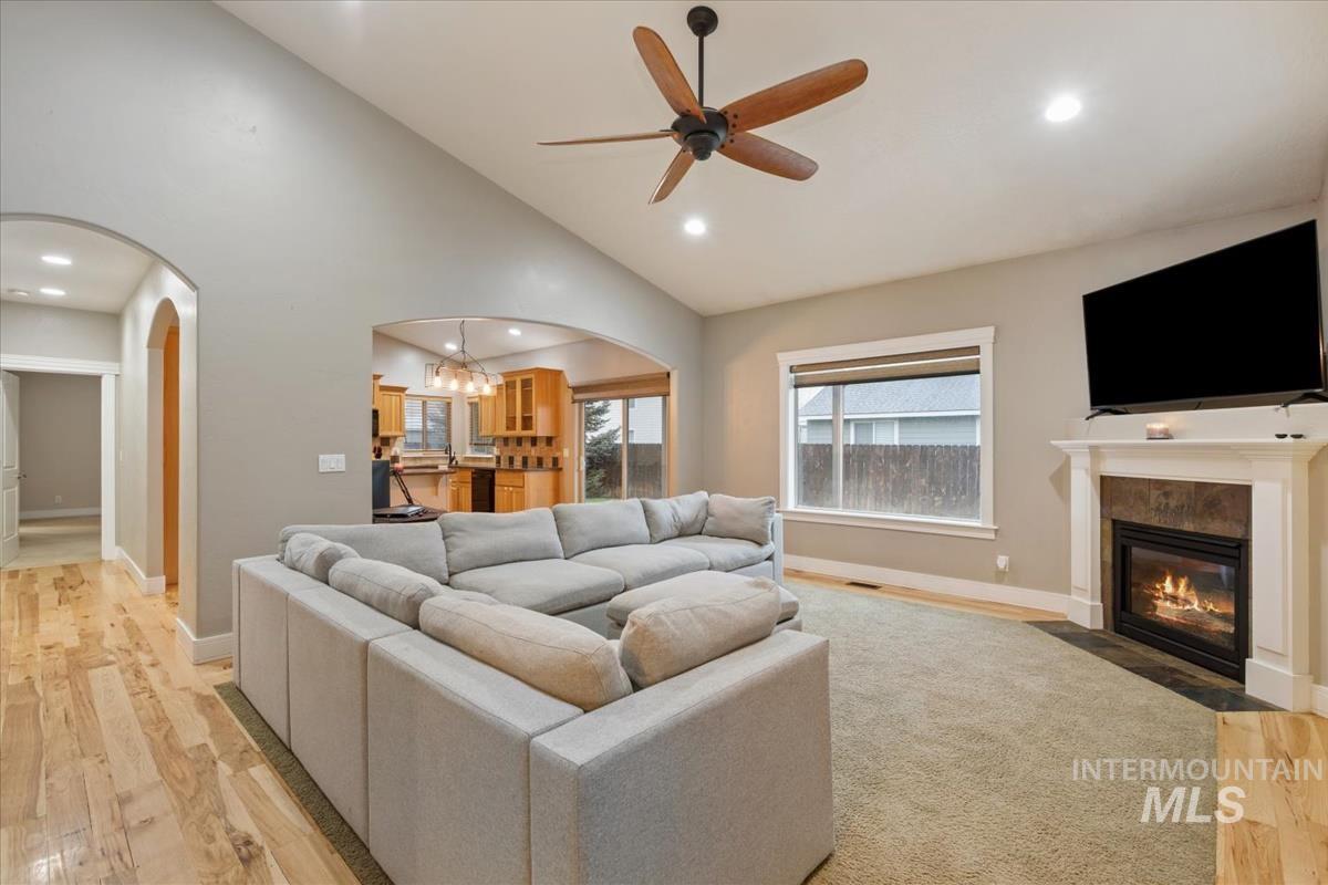 Living area featuring light wood-style flooring, a chandelier, a fireplace with flush hearth, ceiling fan, and arched walkways