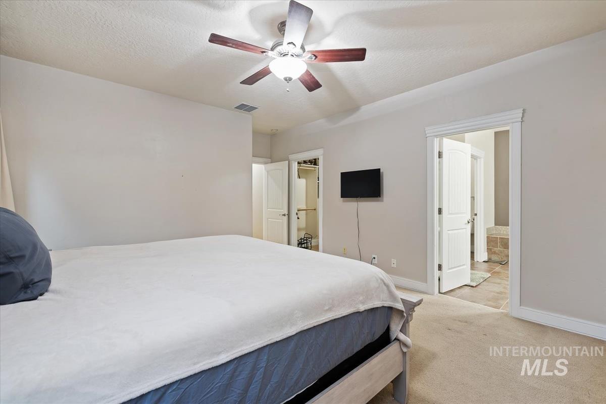 Bedroom with carpet flooring, ceiling fan, a textured ceiling, and a walk in closet