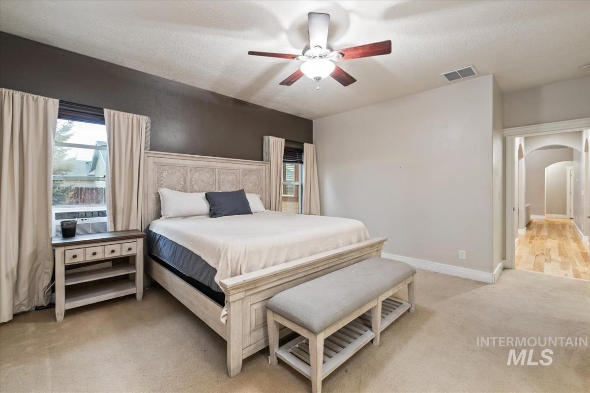 Bedroom featuring arched walkways, multiple windows, light colored carpet, a ceiling fan, and a textured ceiling