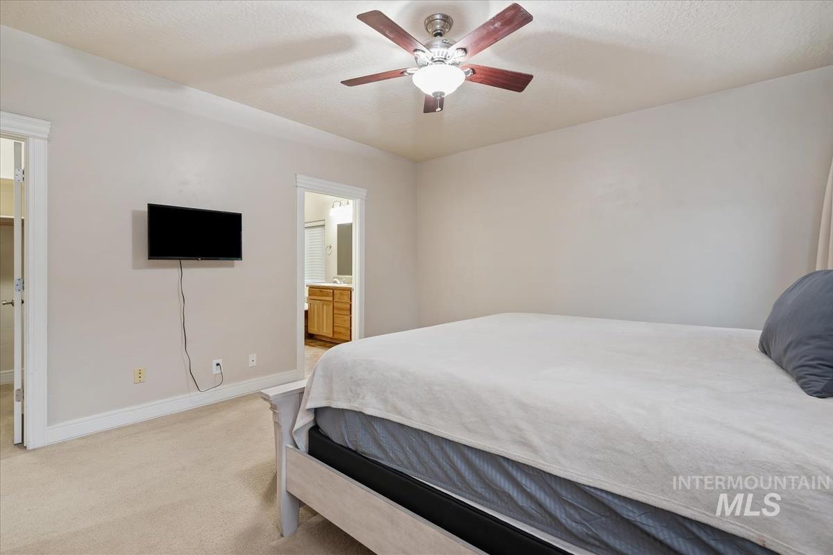 Carpeted bedroom with ensuite bath, a ceiling fan, and a textured ceiling