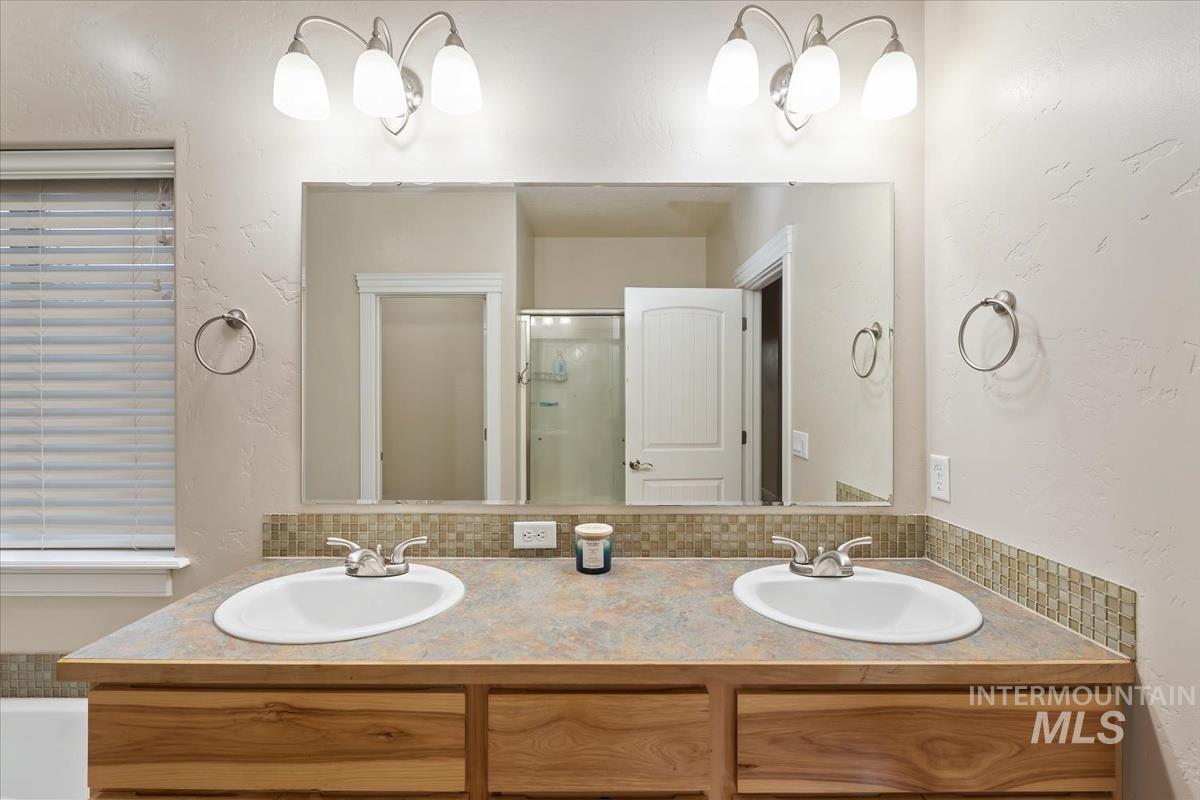 Bathroom with a textured wall, double vanity, and a stall shower