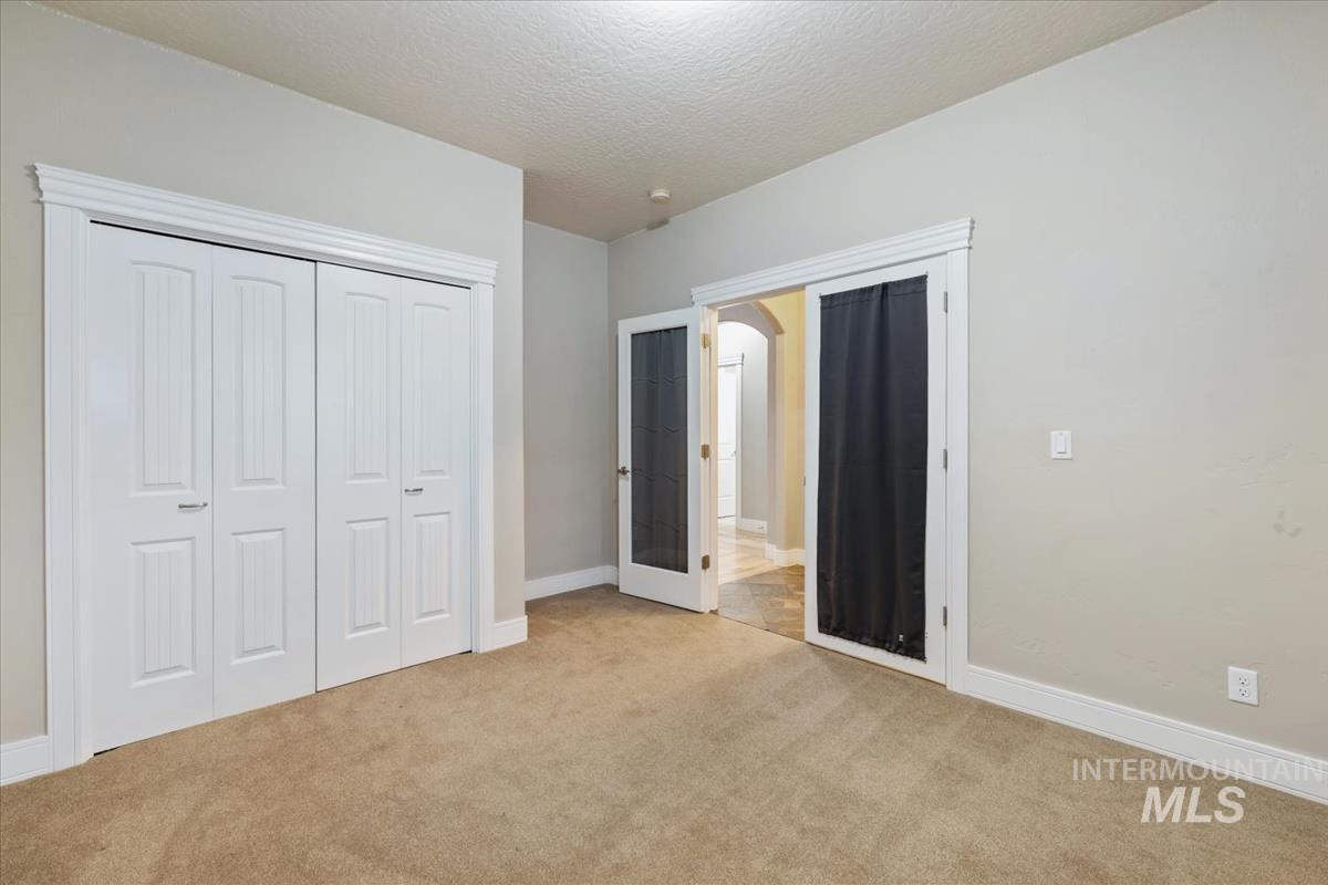 Unfurnished bedroom with carpet, a textured ceiling, a closet, and french doors