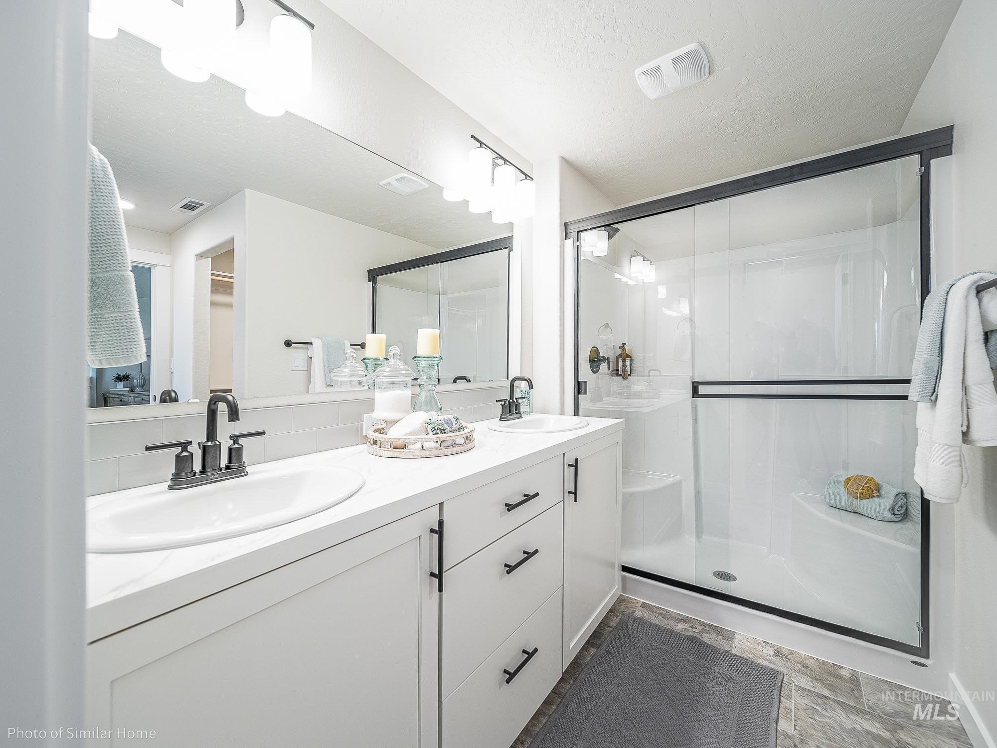 Full bath featuring a shower stall, double vanity, and tasteful backsplash