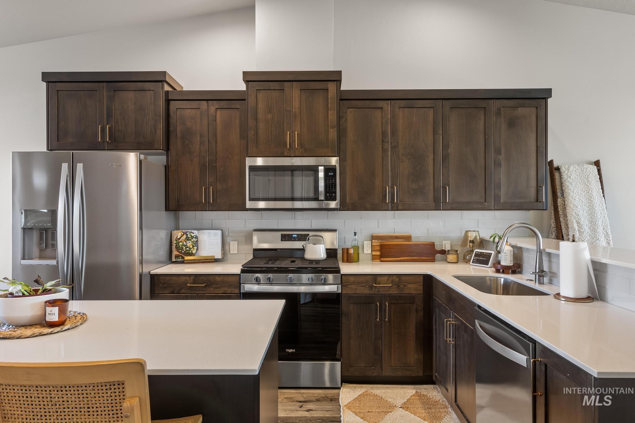 Kitchen with appliances with stainless steel finishes, dark brown cabinetry, tasteful backsplash, a breakfast bar area, and lofted ceiling
